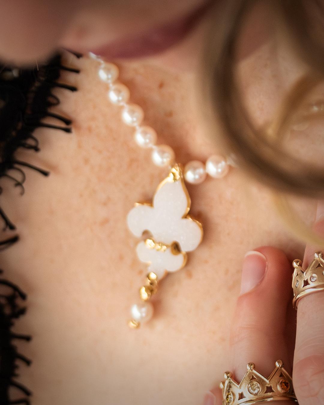 The handmade “Fleur-de-Lis” pendant, made of yellow gold and a crystal agate cut in this shape, has a majestic appearance and is incorporated into a pearl necklace that can be fastened with a gold clasp. 
The playful pearl at the end of the piece is