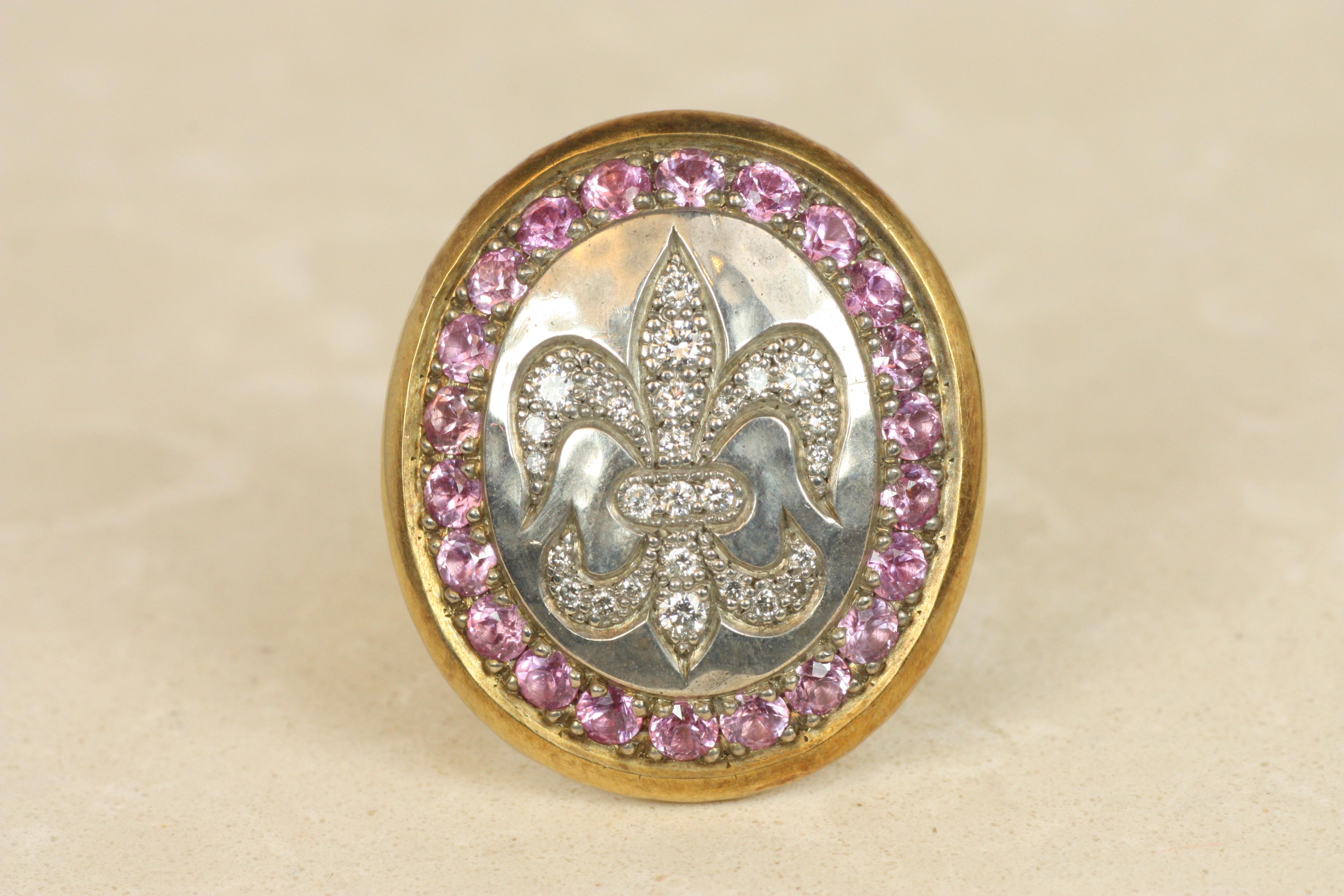 Inspired by heraldic tradition, this striking oval shield ring showcases a fleur-de-lis motif in a shimmering array of diamonds surrounded by vivid pink sapphires. The sterling silver 