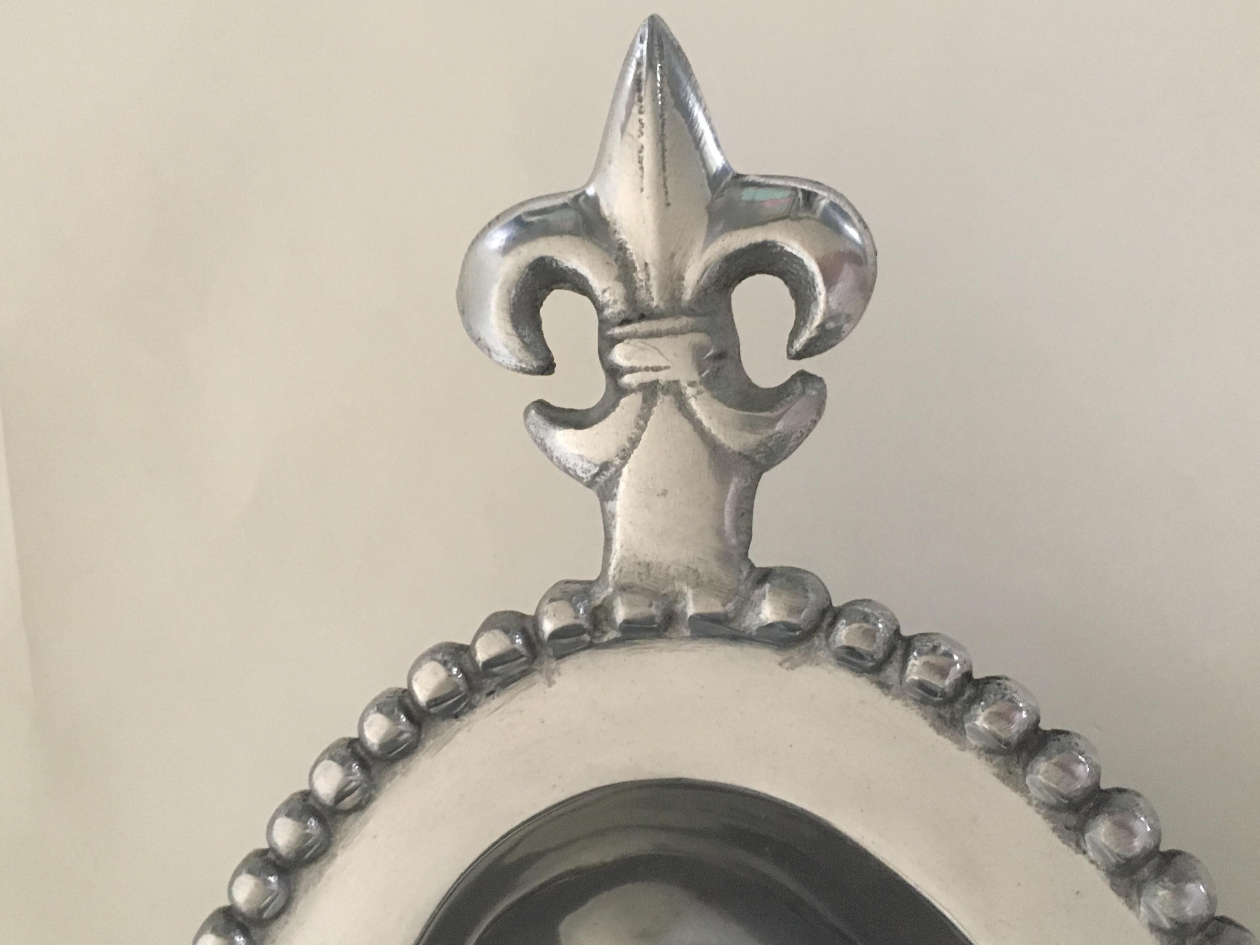 A beautiful silver colored metal serving bowl with fleur de lis handles and hobnail detail around the rim.