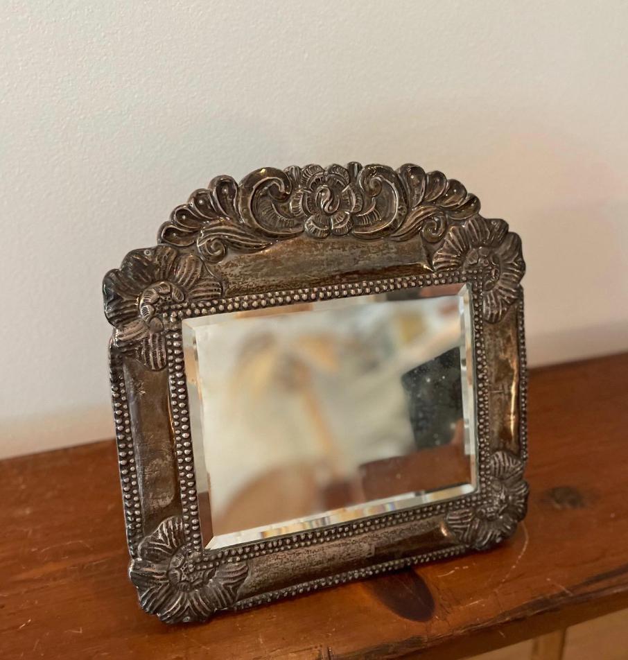  Charming antiqued mirror with Pewter framing with the sweetest floral details. This is a versatile mirror where you can place it on a dresser with it's tail-like stand, or hang it on the wall with included wire. 