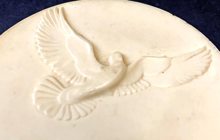 Highly distinctive and unique, this cylindrical paperweight is decorated on its upper surface with exquisitely detailed sculptural relief: a dove in flight, shown flying over a cluster of clouds and the word 