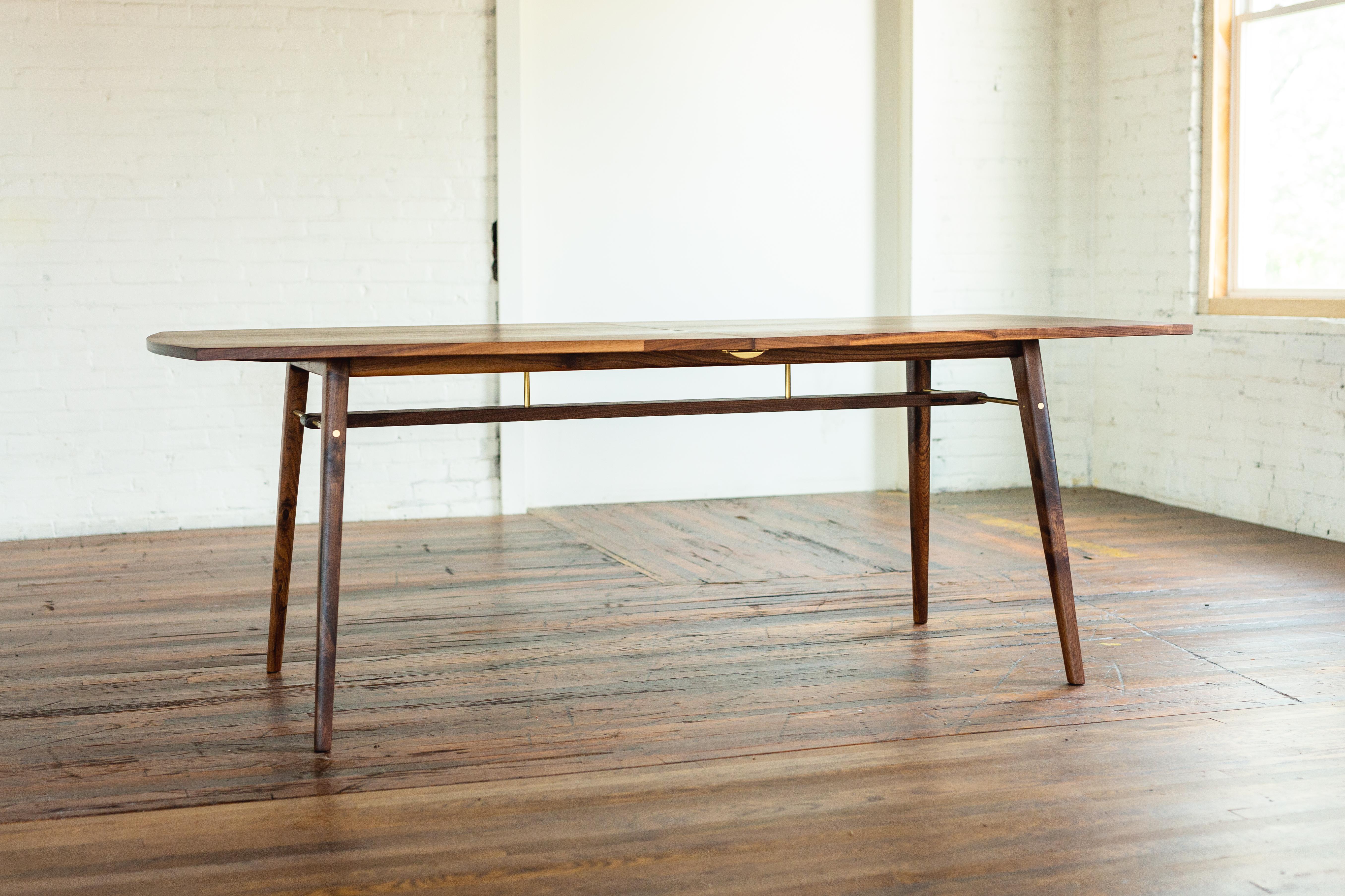 A modern extension table with an abundance of details. Clean lines accented by simple curves.

Solid black walnut wood top and base with detailed brass joinery.
Brass locking hardware to keep the table flush when in closed or extended