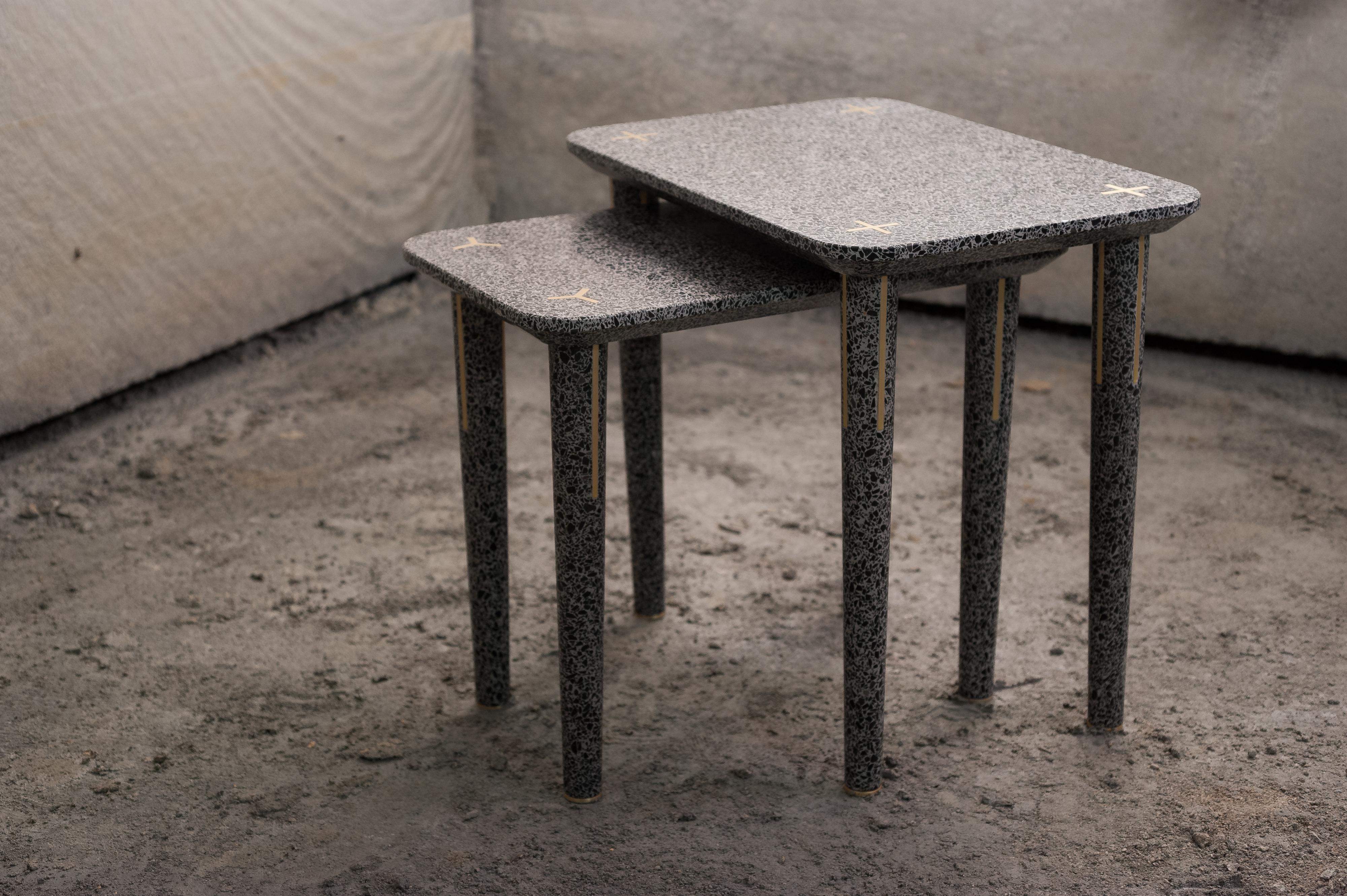Ce design unique est l'une des deux tables gigognes qui font partie de la collection Flint. Fabriquée en terrazzo, un mélange de ciment et d'éclats de marbre, sa silhouette simple est ornée d'inserts métalliques le long des pieds et sur le dessus