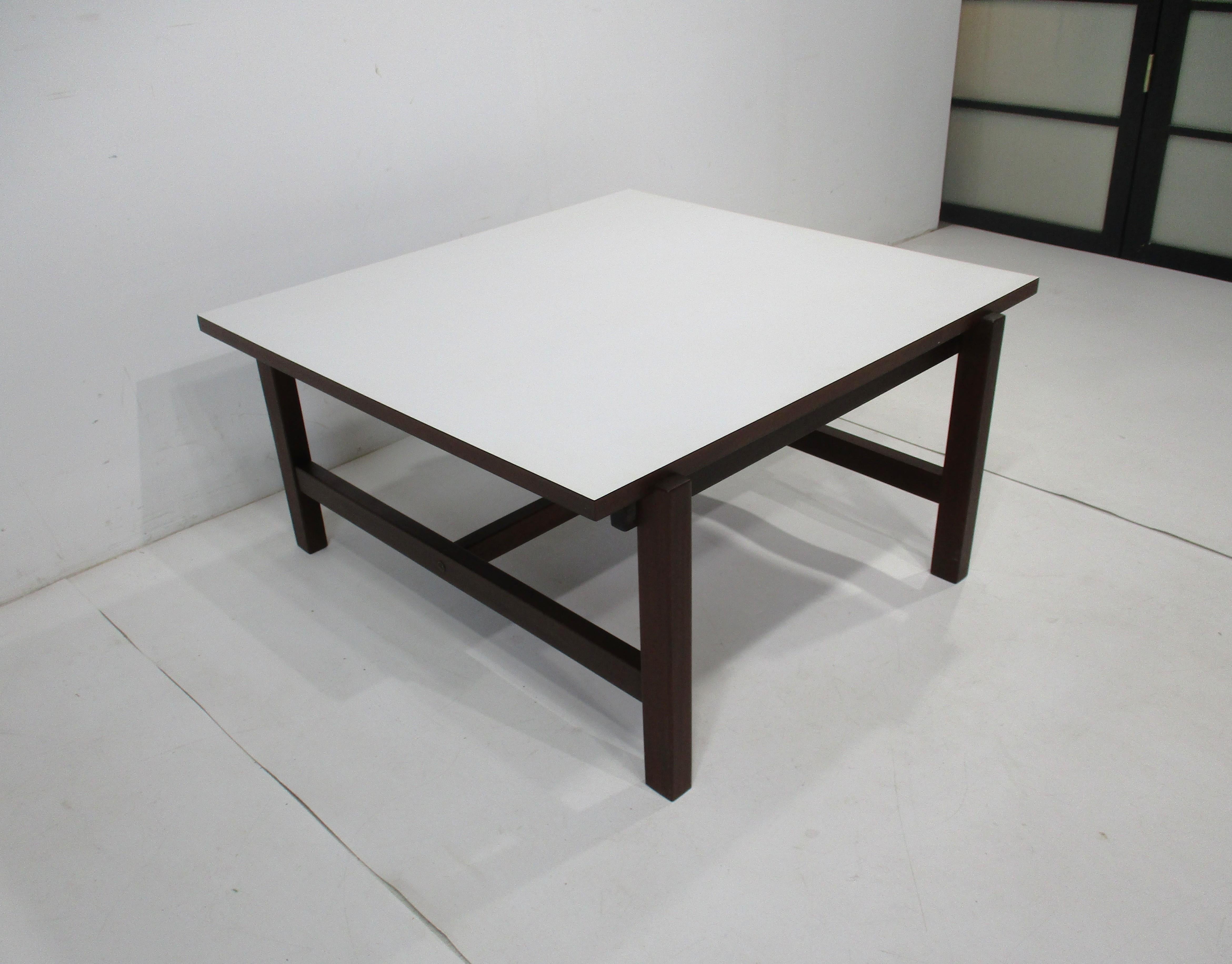 Une table basse fonctionnelle avec un plateau rabattable, un côté est en bois de teck bien grainé et l'autre est en stratifié blanc. La base en teck massif et la structure des pieds entrecroisés rendent la table robuste et très facile à remplacer