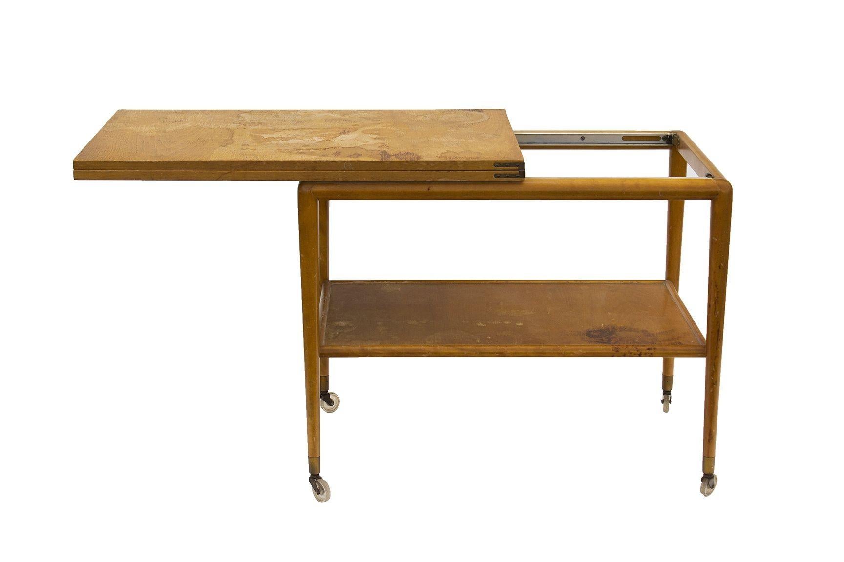 USA, 1953
Flip top serving cart designed by T.H. Robjohn-Gibbings for Widdicomb, model 1779. This is a two level serving cart in what appears to be bleached walnut. The top slides open on a ball bearing track and unfolds to make a surface twice the