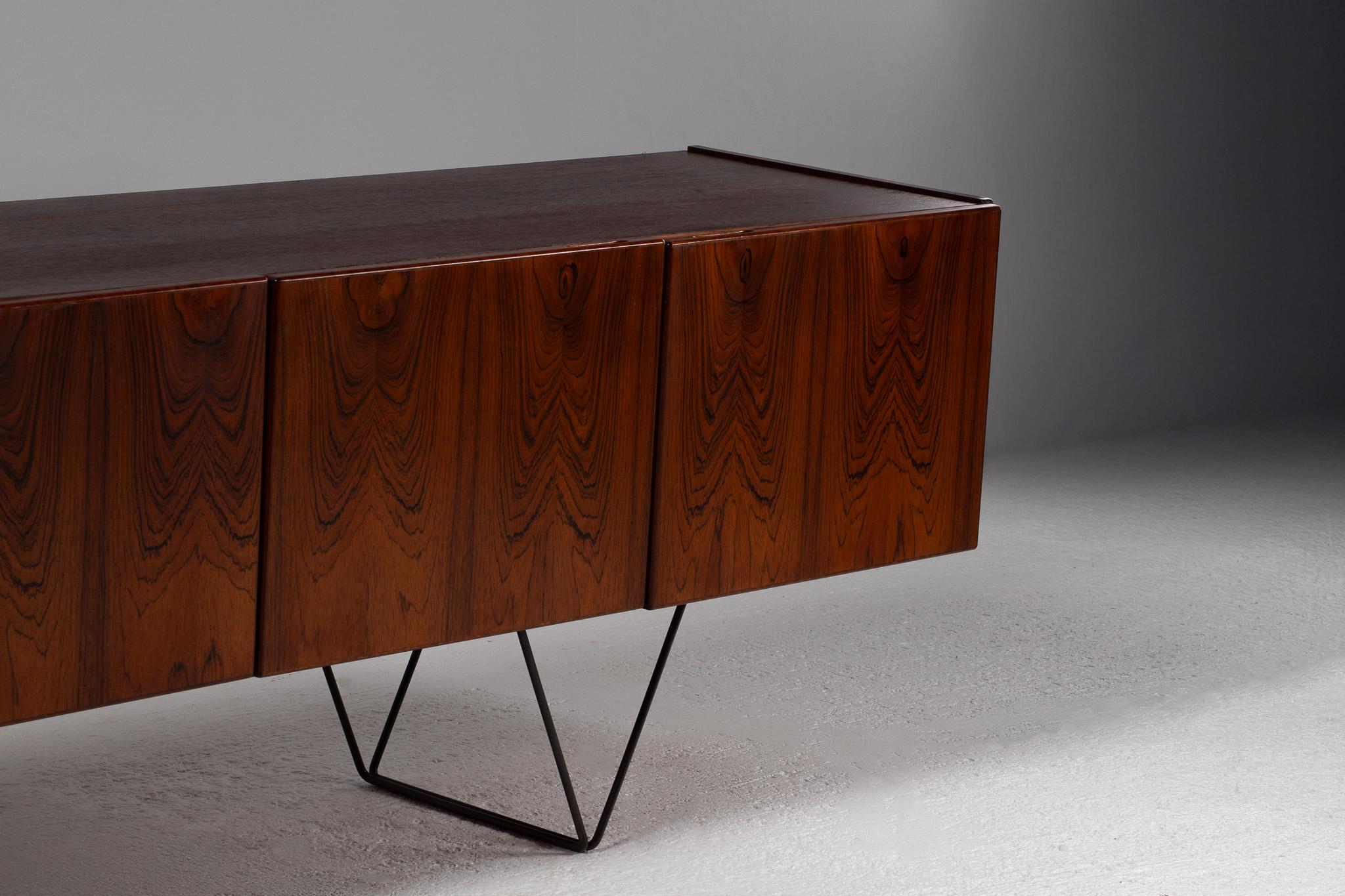 A study in poised elevation, this mid-century modern Italian sideboard appears to hover—its mass of richly figured cocobolo palissander suspended delicately on a skeletal iron base. The visual rhythm is immediate: the flame-like grain of the wood