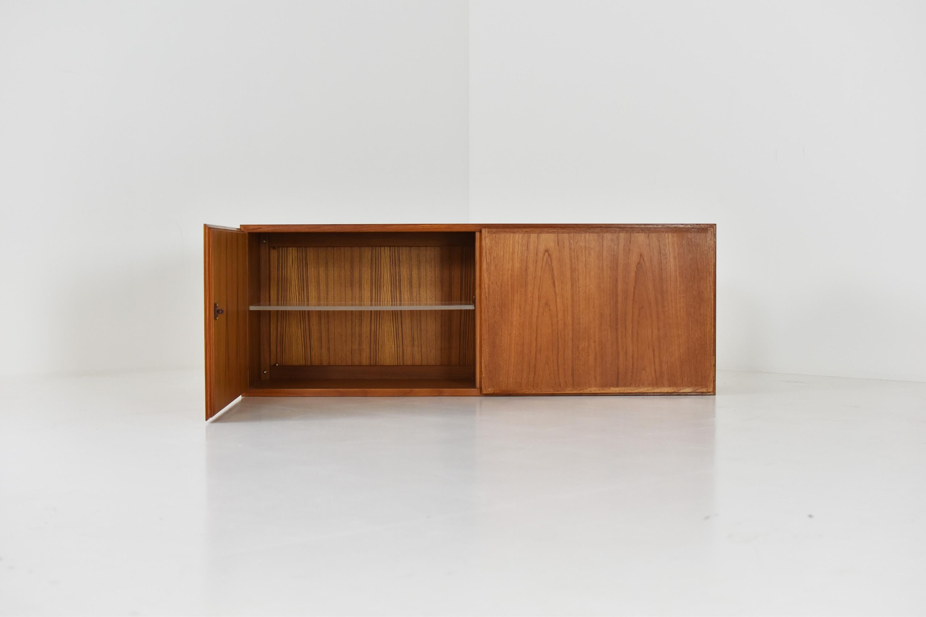 Floating wall cabinet in teak from Denmark 1950’s. This storage cabinet features two storage compartments: on the left a compartment with shelf, on the right an open area. Good original condition. Nice brass details.