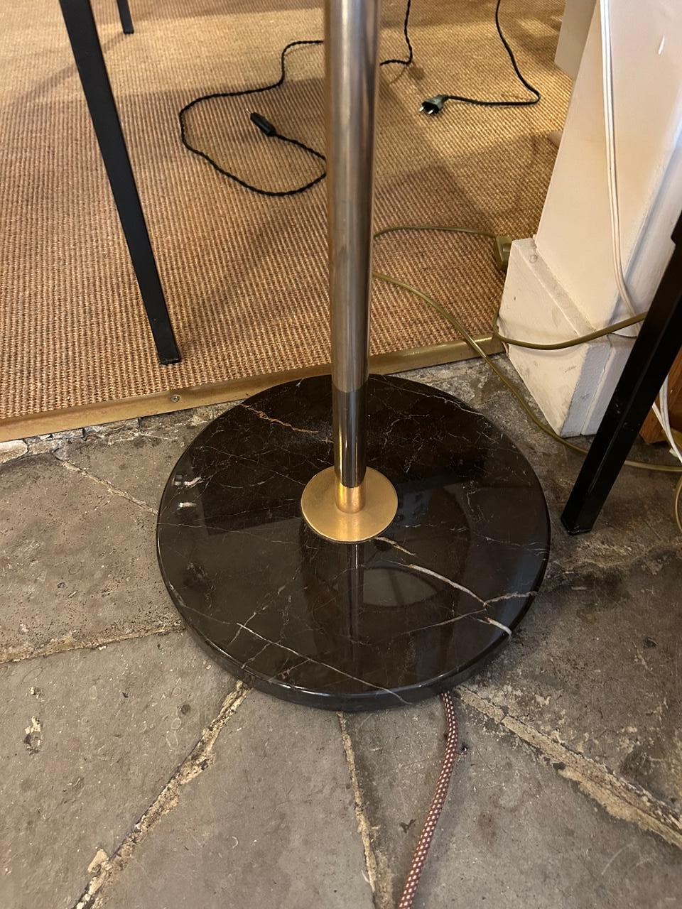 Lámpara de pie con cuerpo cilíndrico de latón patinado, que encierra reflectores de paneles de resina de poliéster cincelada con enganches de latón dorado.
Base de mármol.