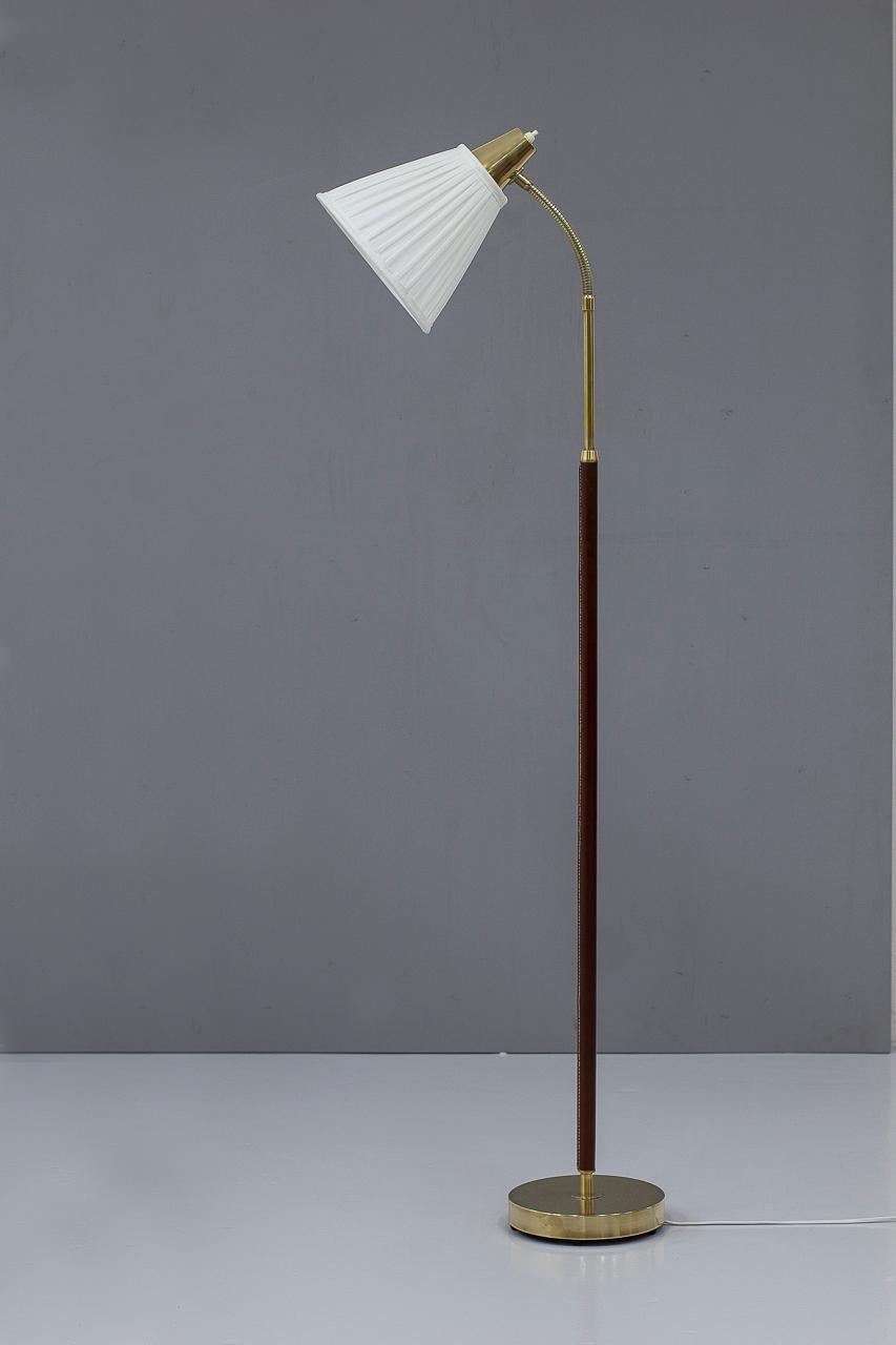 Elegant vintage floor lamp manufactured by Falkenbergs Belysning in Sweden during the 1960s. A stunning piece of lighting that exudes timeless elegance and sophistication. The lamp features a sturdy brass base with a sleek, slender brown leather