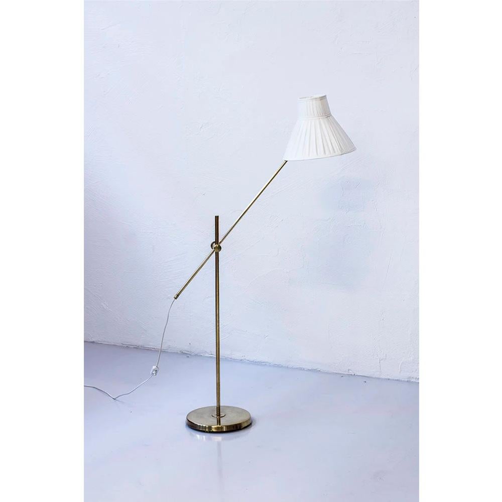 Magnificent and rare height-adjustable floor lamp designed by Hans Bergström. Beautiful patina and assembly of materials with an original cone-shaped lampshade in hand-sewn folded white fabric and polished solid brass structure. Excellent vintage
