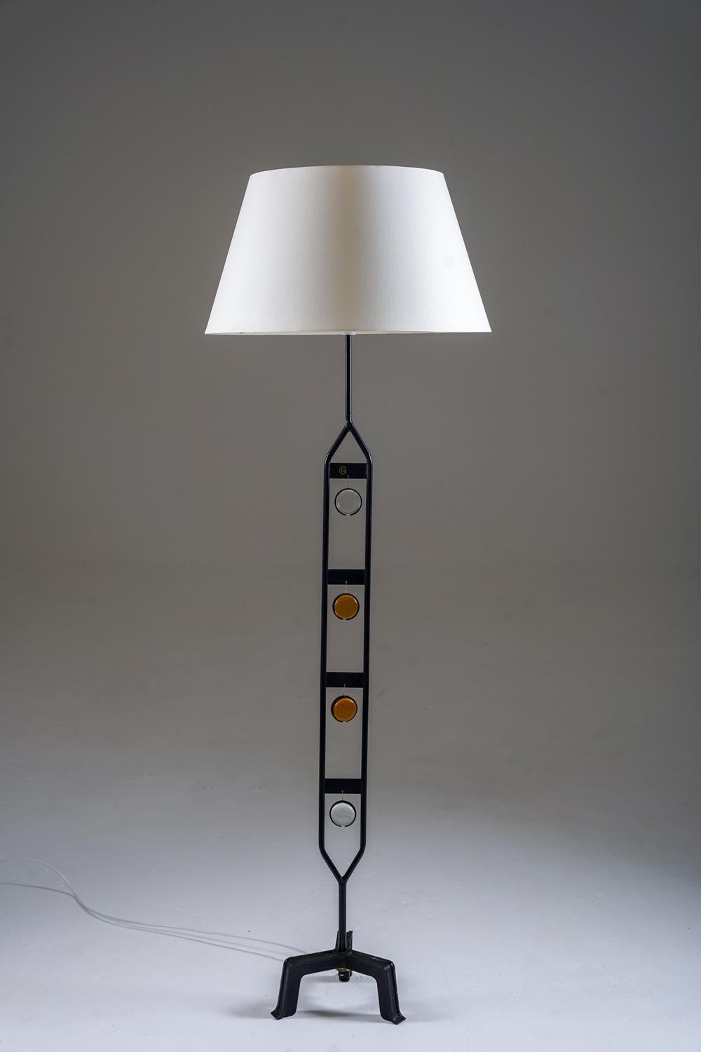 Distintiva lámpara de pie sueca de Nybro Armaturfabrik, diseñada en la década de 1960. La lámpara presenta una escultural estructura de metal negro con recortes geométricos, acentuada por incrustaciones circulares de cristal en tonos claros y ámbar.