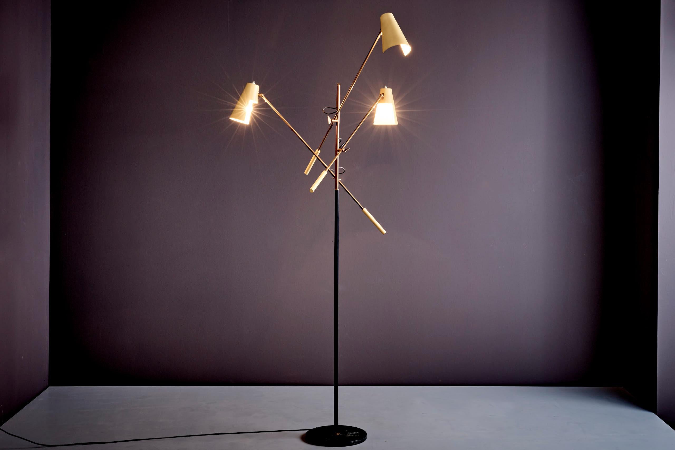 A rare Mid-Century Modern floor lamp by Stilnovo. This sculptural piece features three fully adjustable arms with brass fittings, original cream-colored aluminum shades, and a patinated black marble base. The arms rotate and extend individually,