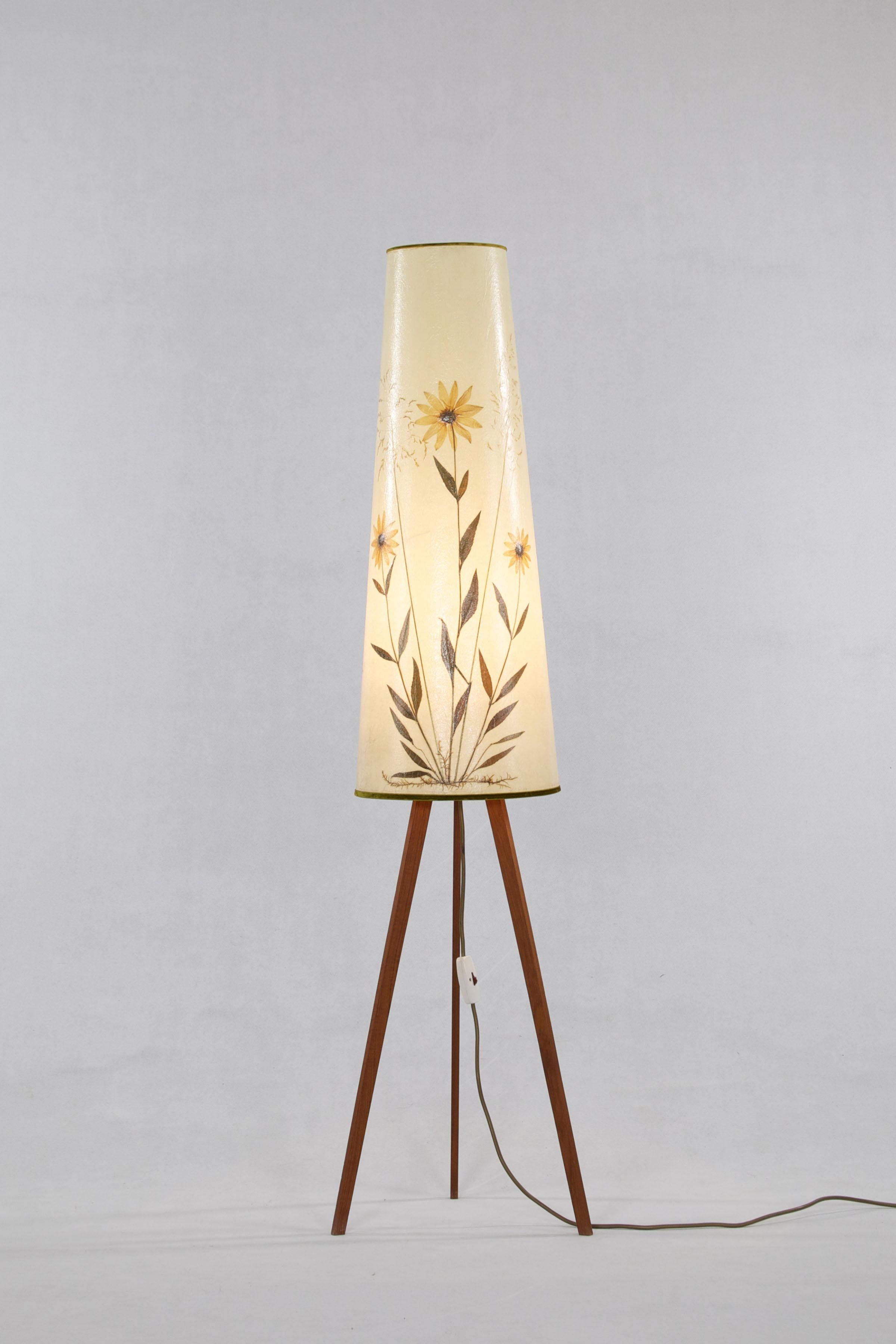 Floor lamp from Denmark, 1960s. This three-legged teak lamp has a hide shade with incorporated dried flowers which cause a beautiful lighting experience. 

Feel free to contact us for more detailed pictures.