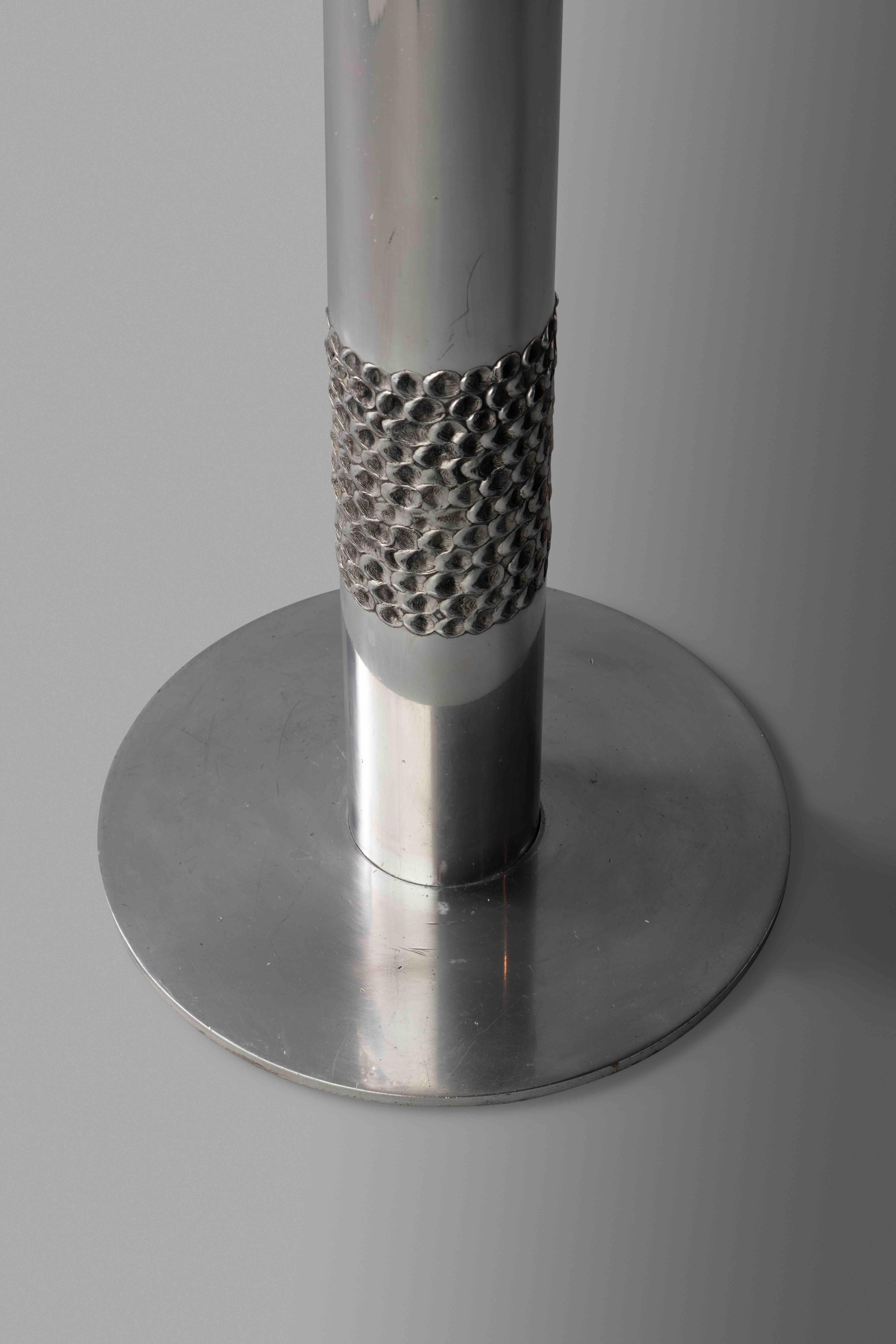 Cylindrical steel body decorated with small circular indented discs.