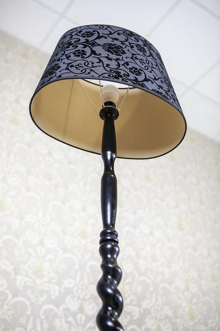 Stehlampe aus dem frühen 20. Jahrhundert mit floralem Stoffschirm

Stehlampe mit Holzgestell und Lampenschirm aus Stoff. Der Lampenstiel ist spiralförmig gedreht und steht auf einem runden Sockel mit Beinen. Der Lampenschirm ist mit einem floralen