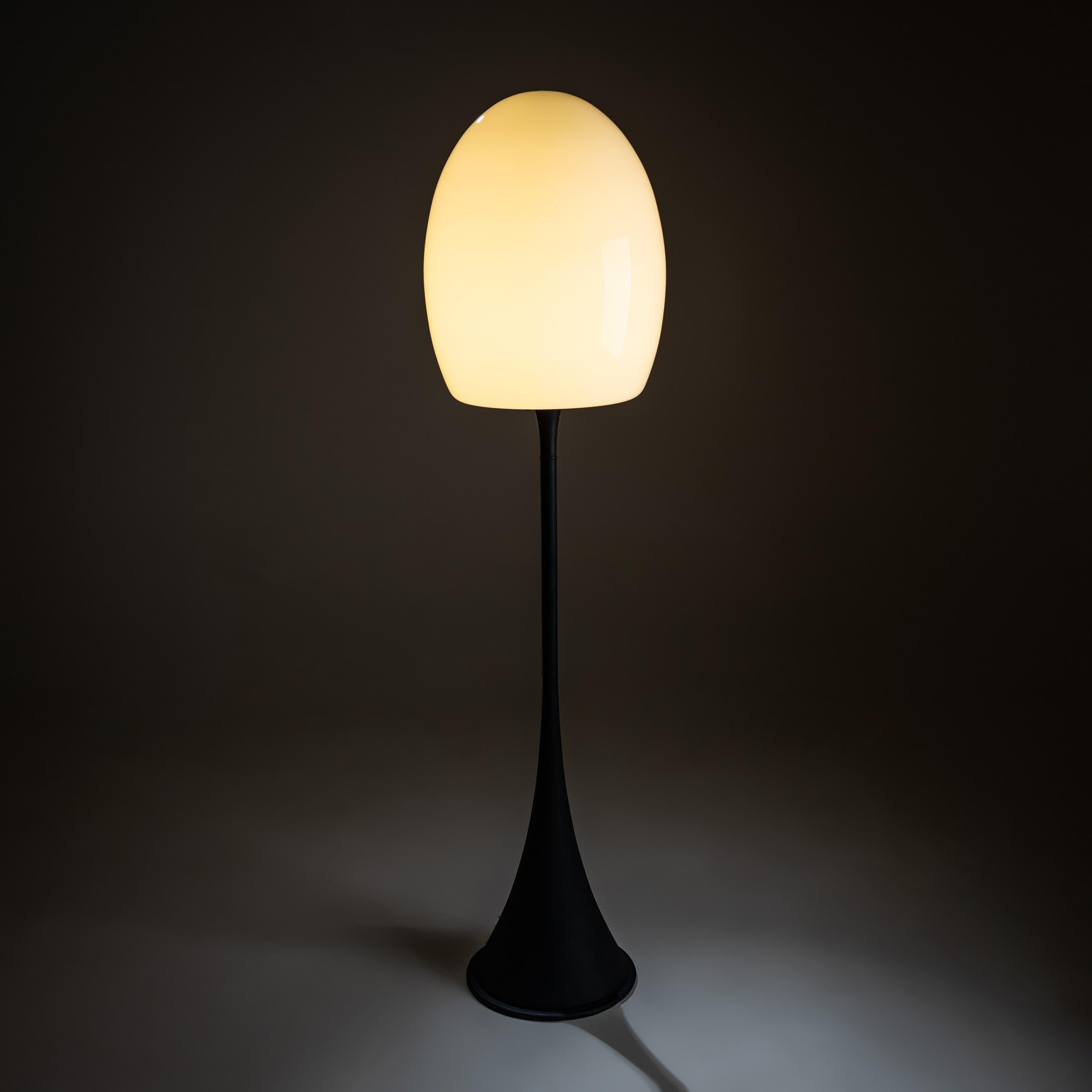 Lámpara de pie con una pantalla orgánica en forma de seta de cristal blanco opalino sobre una base cónica lacada en negro. La pantalla de cristal soplado a mano emite una luz suave y difusa, creando un resplandor atmosférico. Necesita recableado. 