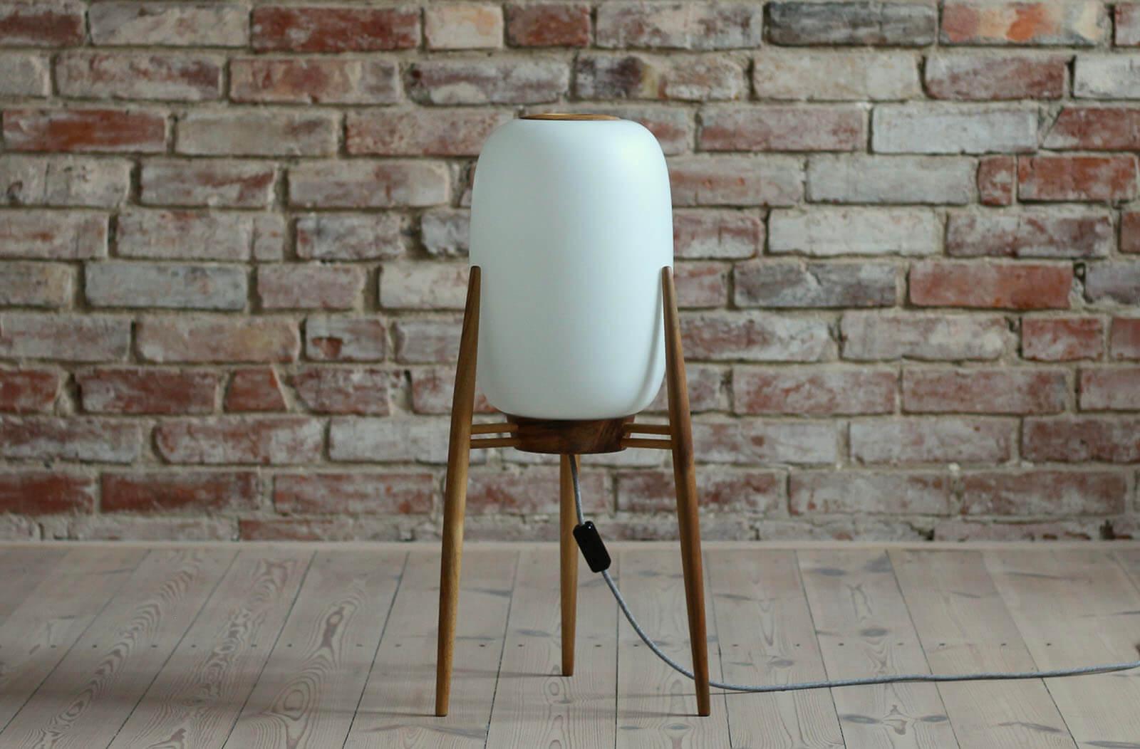 This Space Age floor lamp was produced in the 1960s in Czech Republic. It features a beautifully shaped wooden tripod base and a milk - white glass lampshade. The lamp gives a soft and warm light creating pleasant atmosphere in the room. The