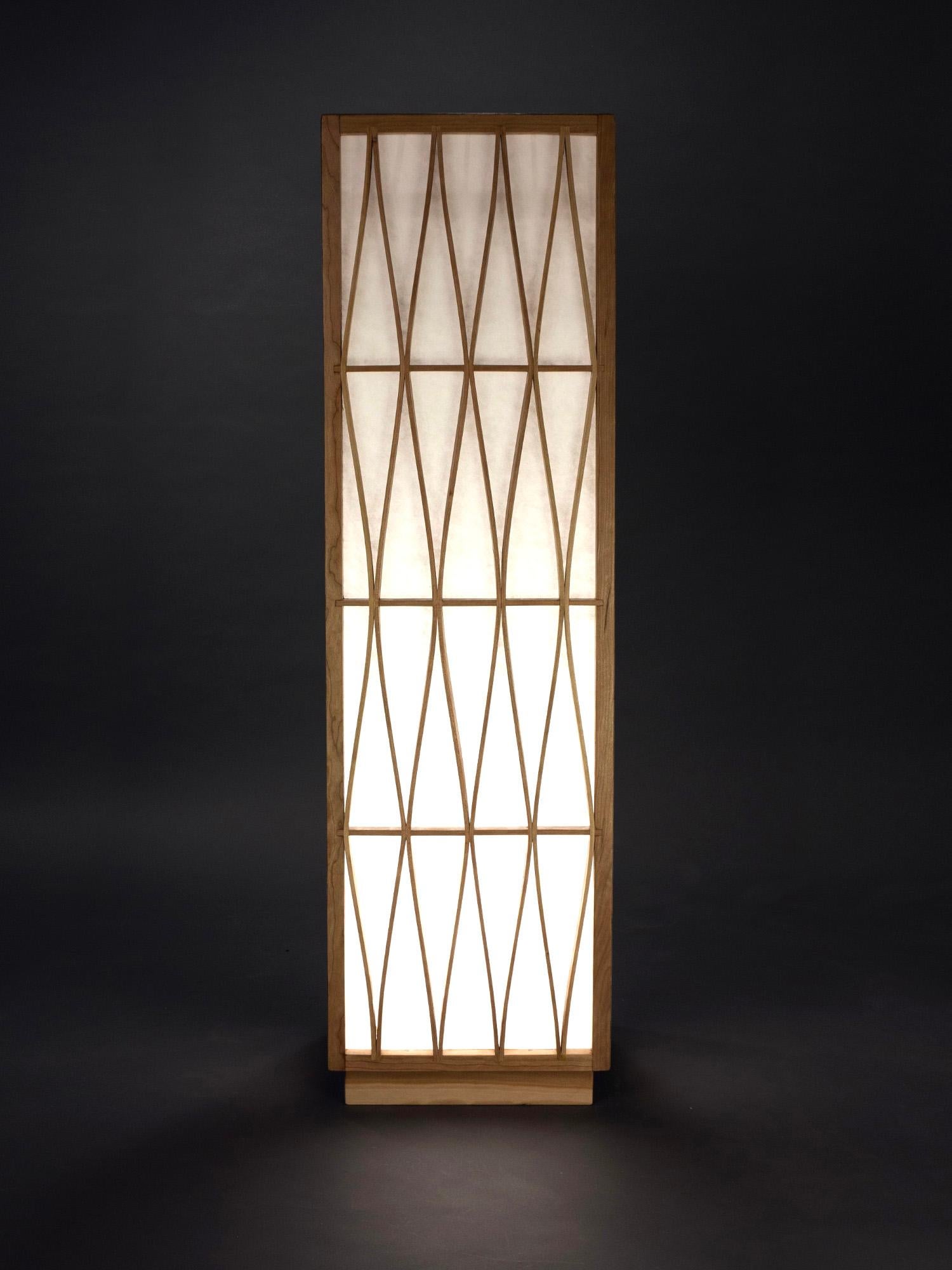 The Skyscraper Floor Lamp stands 4 feet tall with an external architectural structure made from cherry wood. Its external frame provides strength, while protecting the internal Shoji paper screens. Shoji is a traditional Japanese paper made from