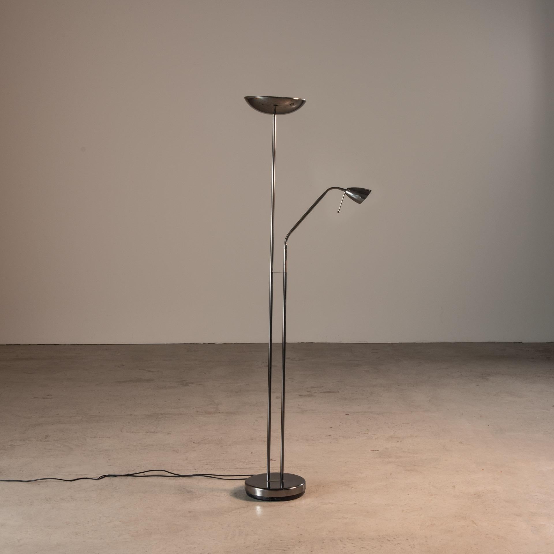 This mid-20th century floor lamp features a sleek design typical of the era, with a focus on functional simplicity and the use of modern materials such as steel and chrome. The lamp has a dual-lighting feature, with one large, inverted bowl-like