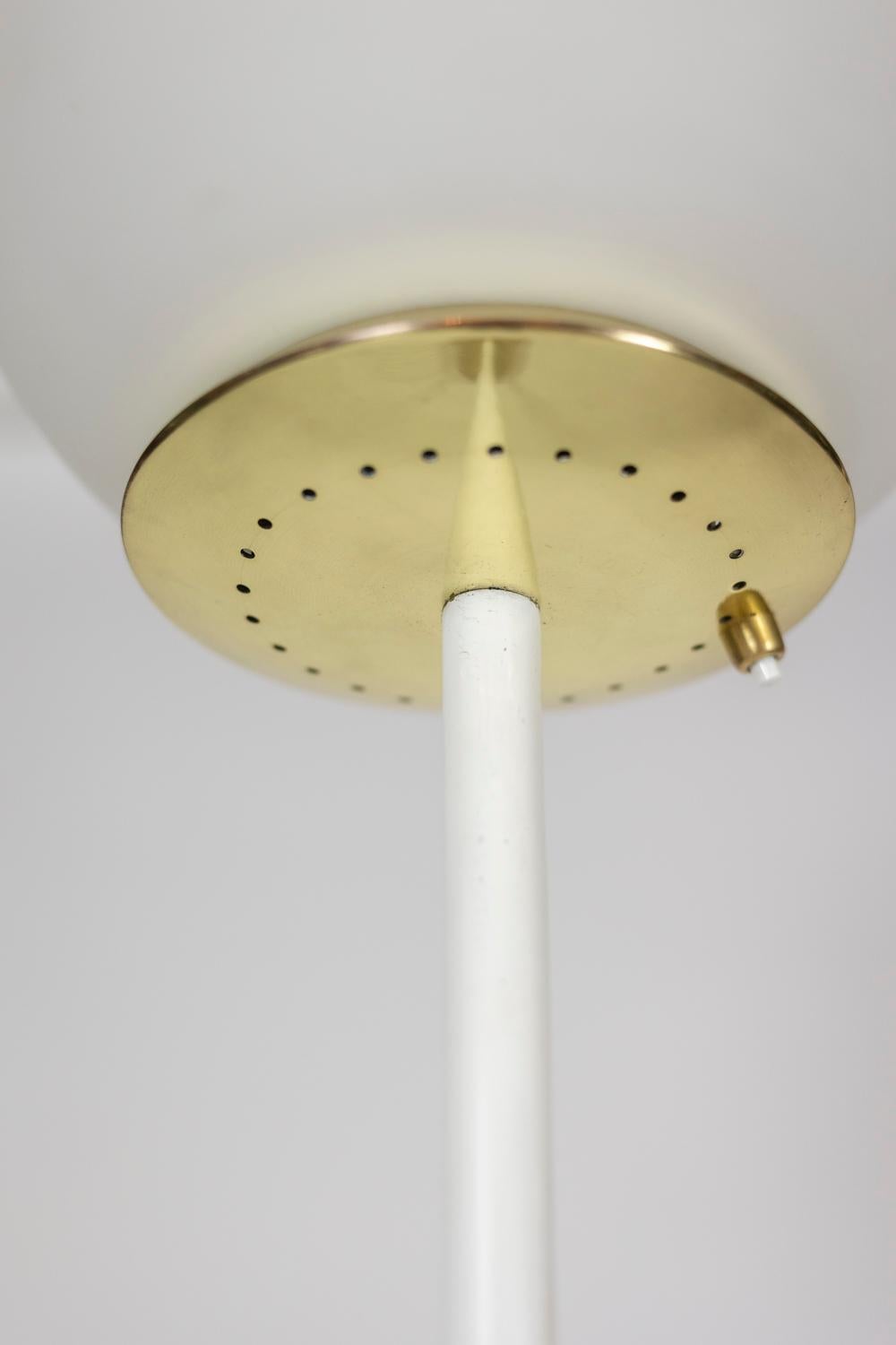 Floor lamp made of white opaline surrounded by gilded and perforated brass, with its white lacquered metal shaft resting on a circular travertine base.

Italian work realized in the 1950s.

Reference: LS5923588I