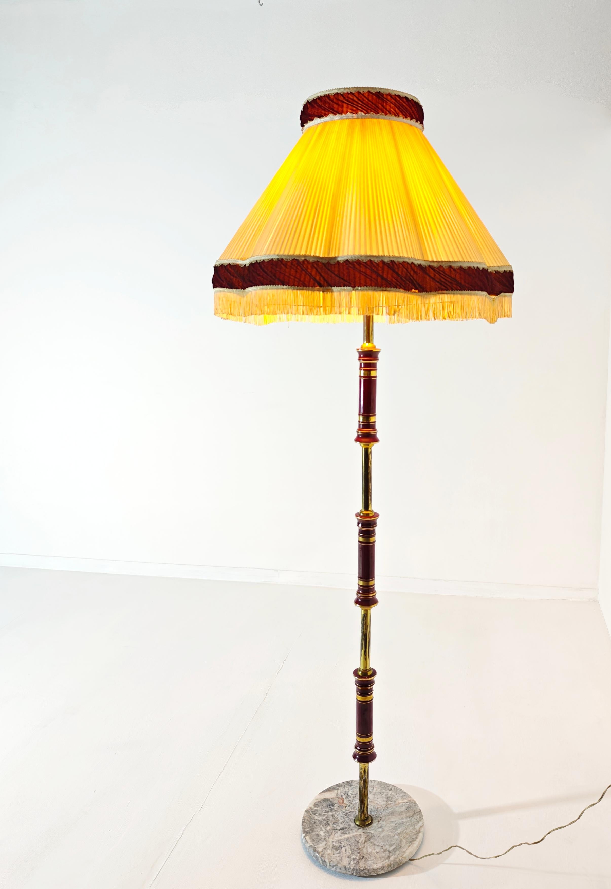 Lámpara de pie de tamaño considerable. Fabricado en Italia en los años 40/50. Base circular de mármol. Vástago de latón con partes decoradas en tonos burdeos. Pantalla plisada de terciopelo y beige. Tres luces con interruptor colocadas en el