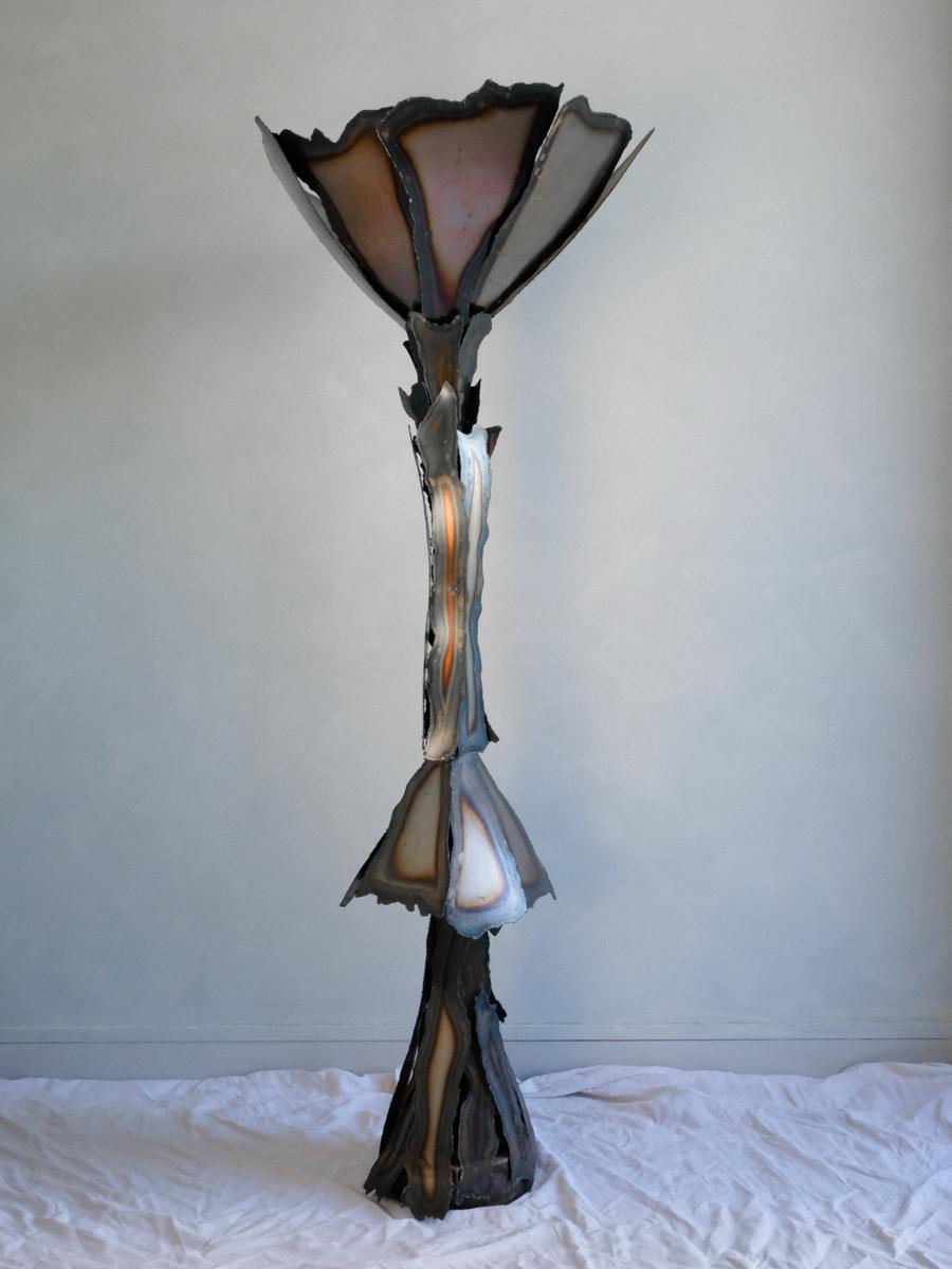 Floor lamp made of cut and oxidized steel sheets stylizing a flower, anonymous work from the 1980s, French production, 72 cm x 190 cm. 

This stylized work shows an overflowing imagination where nature seems to be captured in full movement. The