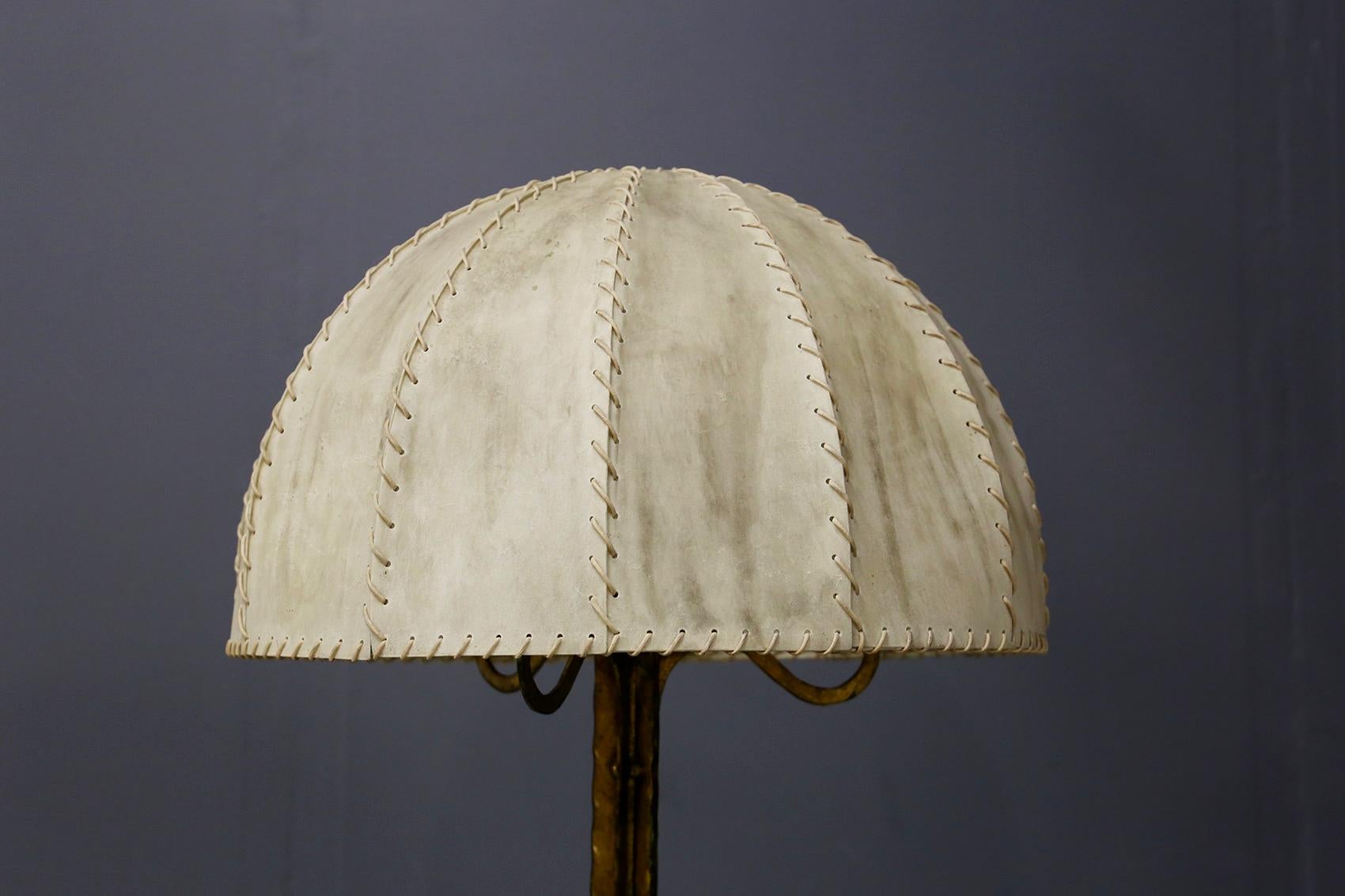 Elegant French floor lamp by Marc Du Plantier in very good condition. The lamp has a semi-circular hat covered in parchment and sewn together by a cotton thread. The structure of the lamp is made of brass worked not regular. The base of the lamp is