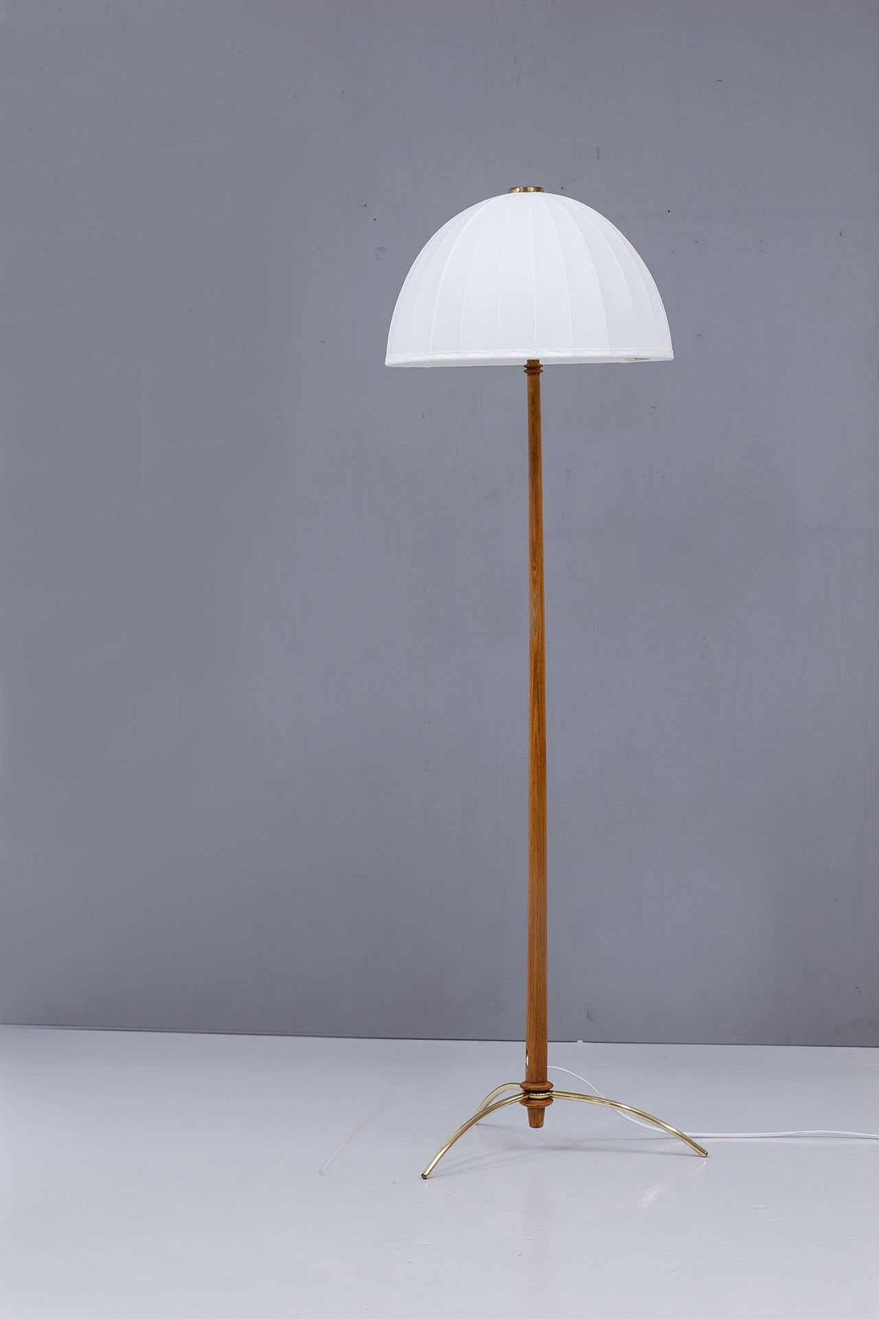 Vintage floor lamp, model G45, designed and manufactured by Hans-Agne Jakobsson in Sweden during the 1950s. The lamp features a stained beech stem and a brass tripod base, it comes with its original lamp shade that has been reupholstered in