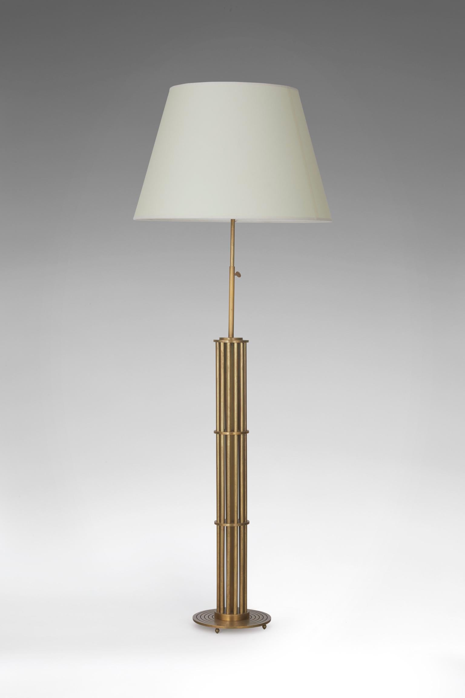 With a patinated brass base composed by tubes forming a cylindrical cage on a circular flat grooved base. Adjustable height from 47.2-53.2 in with the lampshade.