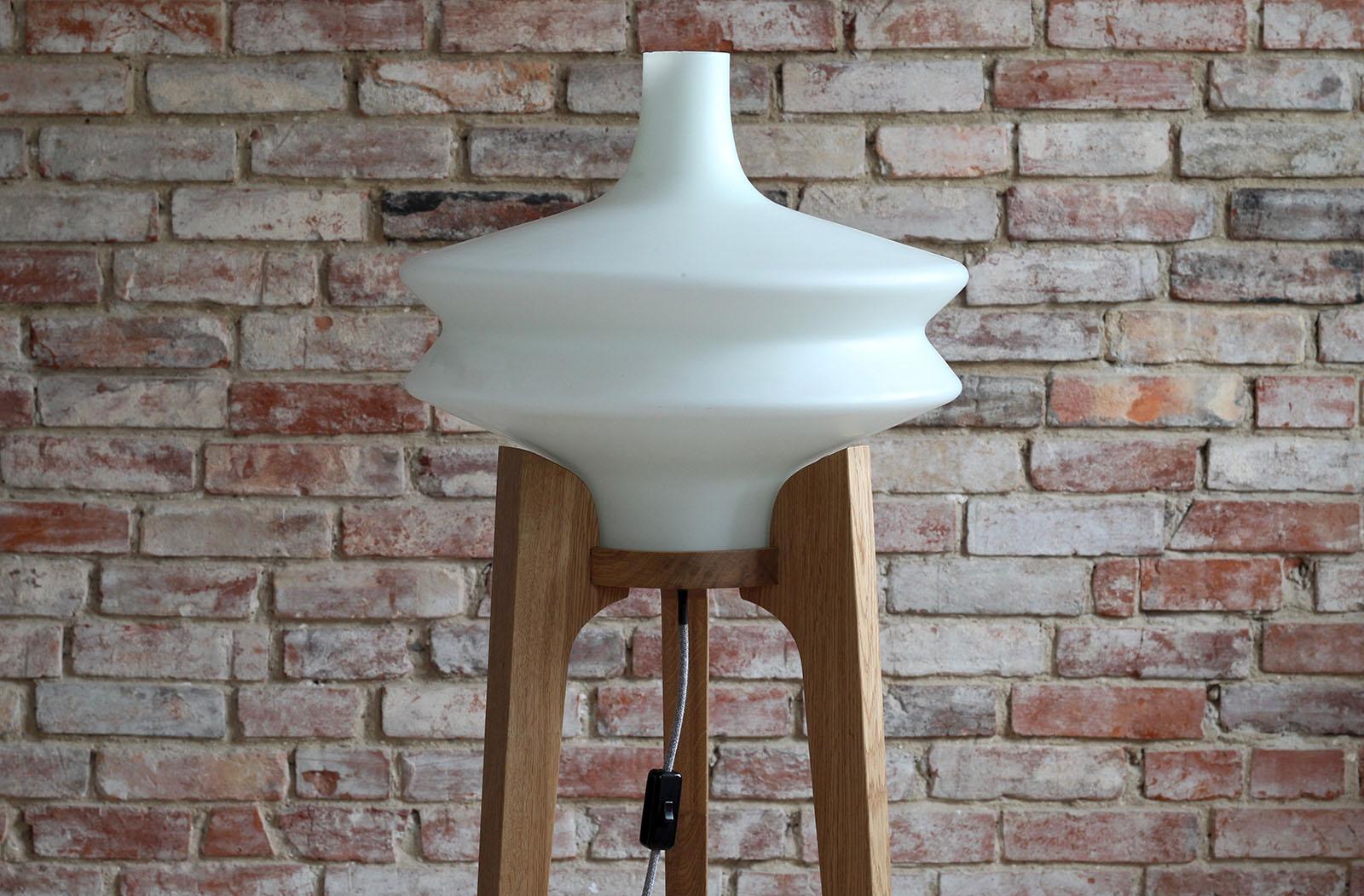 This 1960s floor lamp was made by Czech manufacturer Uluv (Ustredi lidove a umelecke vyroby). It has a large milk-white glass lampshade set on a three wooden legs base. It gives a warm delicate light creating good vibes in the room. The wooden base