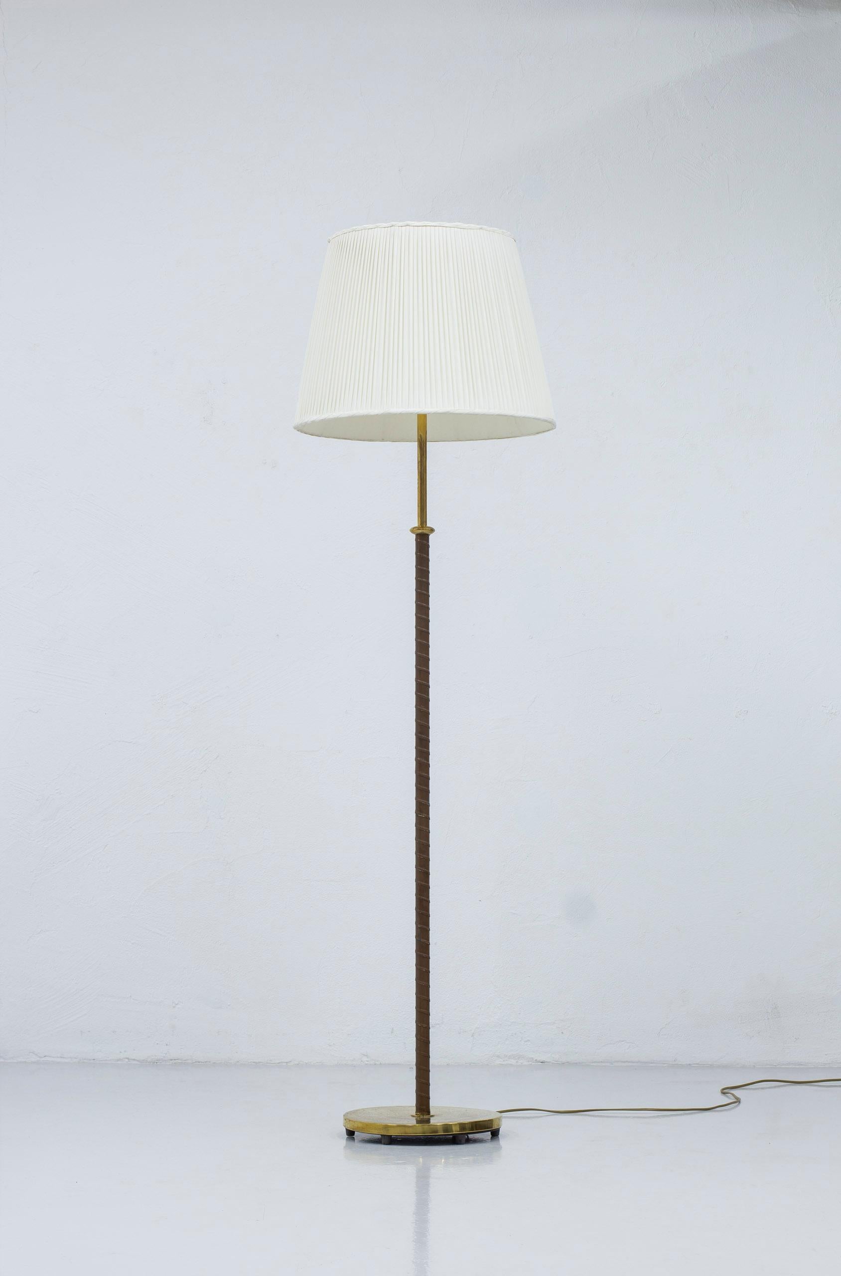 Floor lamp model 15600 designed by Harald Notini. Produced by Arvid Böhlmarks lampfabrik. Made during the 1950s. Brass and wrapped stem with original leather. Large hand pleated silk shade. Original bakelite turn switch on the lamp holder in working
