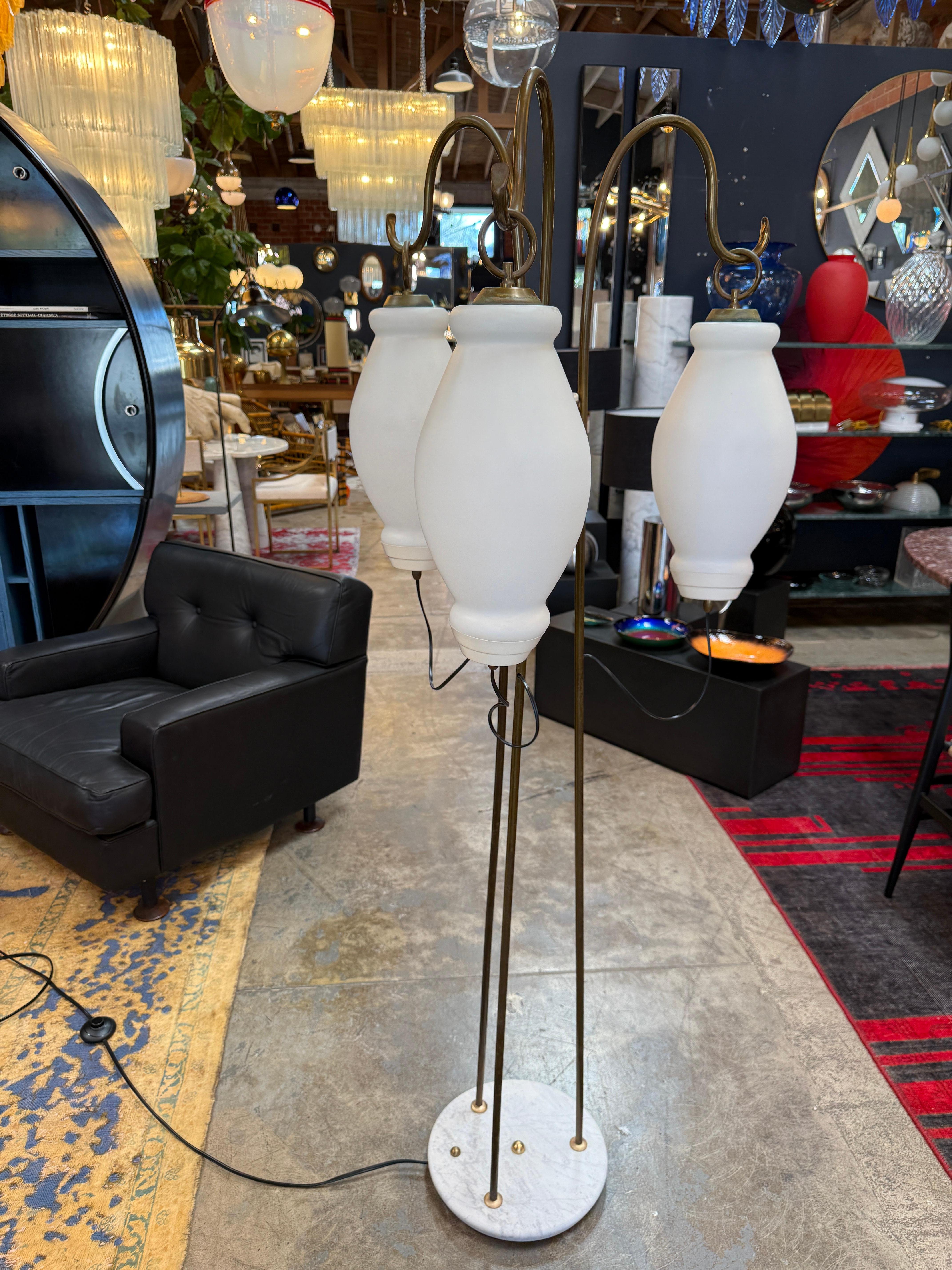 Elegant lampadaire italien des années 1950, présentant trois bras en laiton gracieusement arqués qui suspendent chacun un sculptural abat-jour en verre opalin. Les diffuseurs en verre blanc diffusent une lumière chaude et douce, équilibrée par la