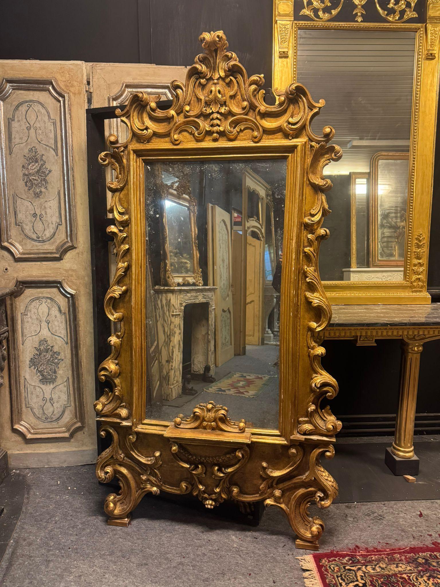 Antique floor mirror in gilded wood, richly carved with scroll decorations, original from the 19th century, from Italy.
It was placed at the entrance of an elegant noble residence, it has a particular central shelf where you can put a light to