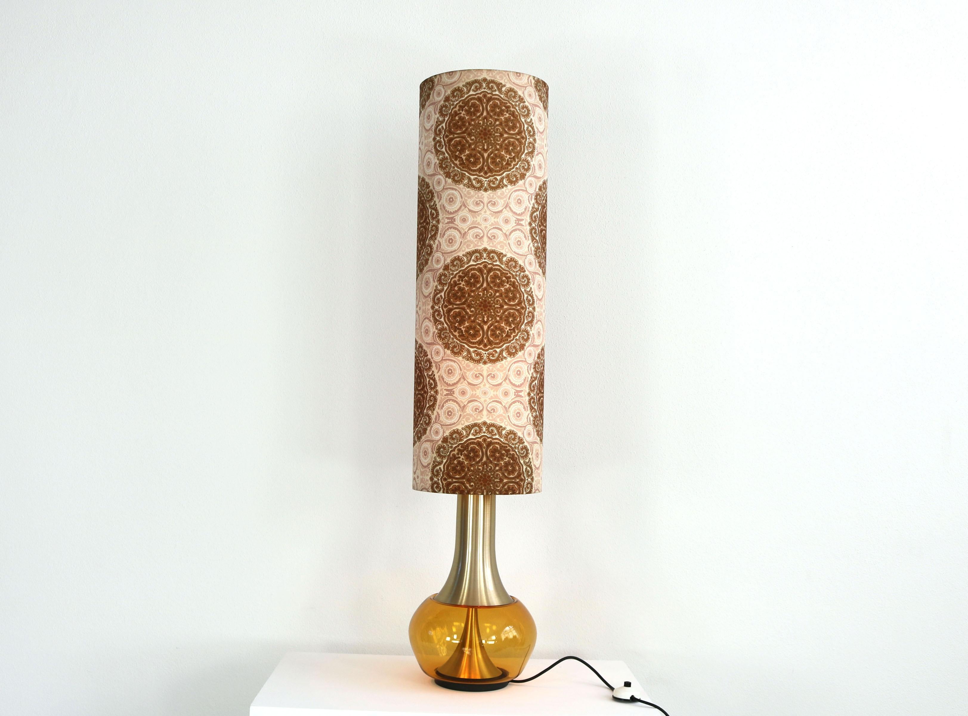 This floor lamp was made in the 70s. It consists of an illuminated glass base and a fabric shade with a floral pattern. The lamp can be switched separately in 3 ways - base only, shade only or both together. Manufacturer: Doria, Germany.