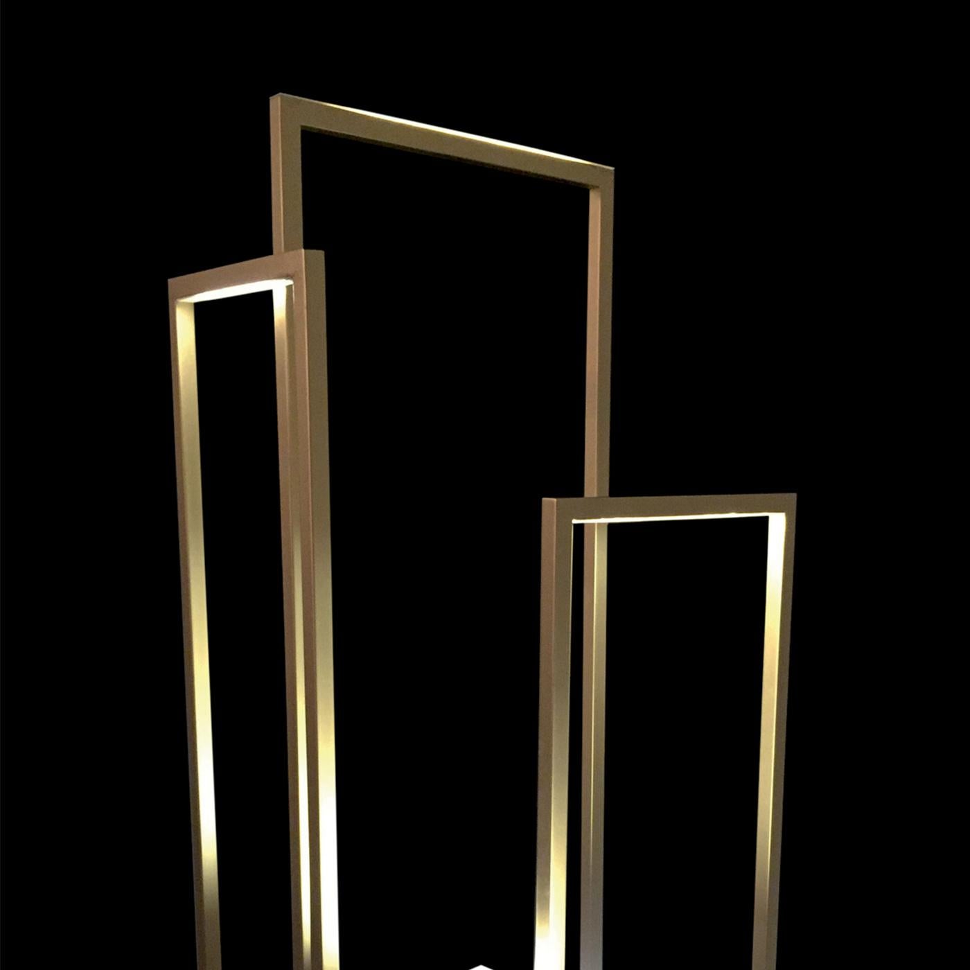 This modern floor lamp is made of several bars in gold finish iron with a square section that cross at different heights, creating a series of rectangles positioned in different directions. LED lights run around the inner perimeter of the bars