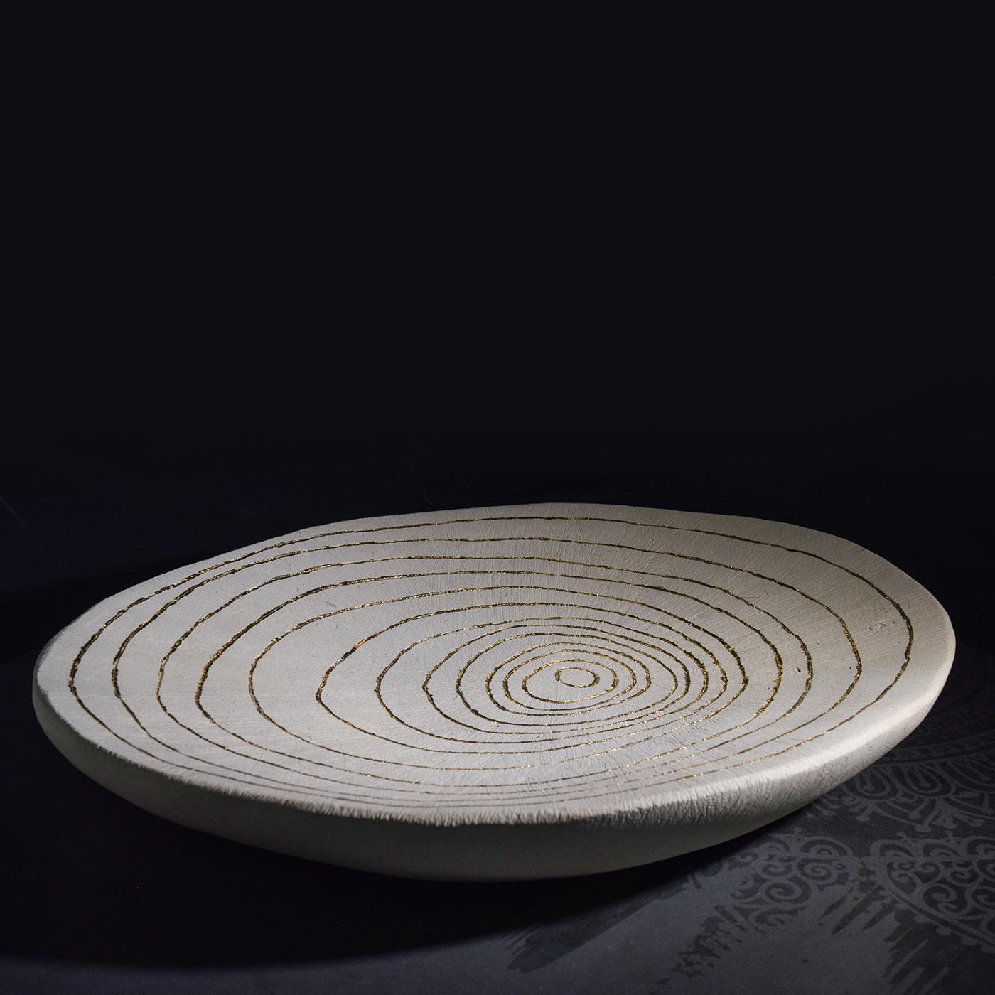 This superb bowl from the Flora Collection is crafted of Lecce stone with a shallow shape and boasts an engraved, concentric circle design enriched with gold leaf. Exclusively handmade, this piece is distinguished by its unique material, a type of