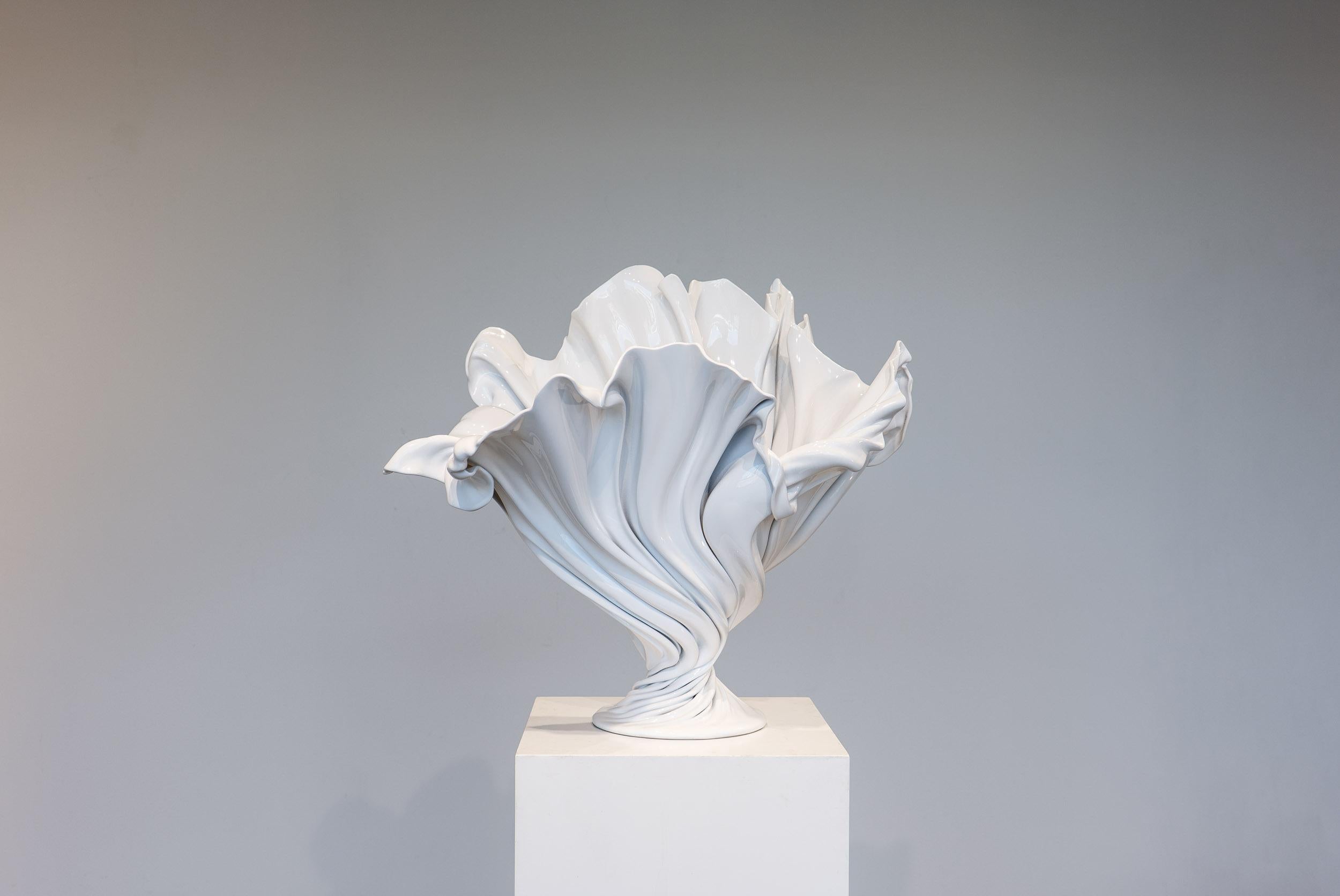 An ode to movement stilled in time, the Flora Vase evokes the fluid grace of petals caught mid-bloom. Its surface, rendered in a luminous gloss white, captures and distorts light across sweeping folds that seem to unfurl and twist from a central