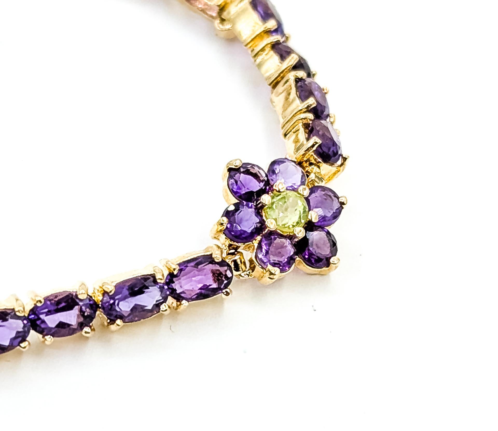 Dieses farbenfrohe Armband ist aus 14-karätigem Gelbgold gefertigt und zeigt ein anmutiges, florales Tennismuster, das mit violetten Amethysten und leuchtend grünen Peridots verziert ist. Die Amethyste haben insgesamt ca. 8,8 Karat und werden durch