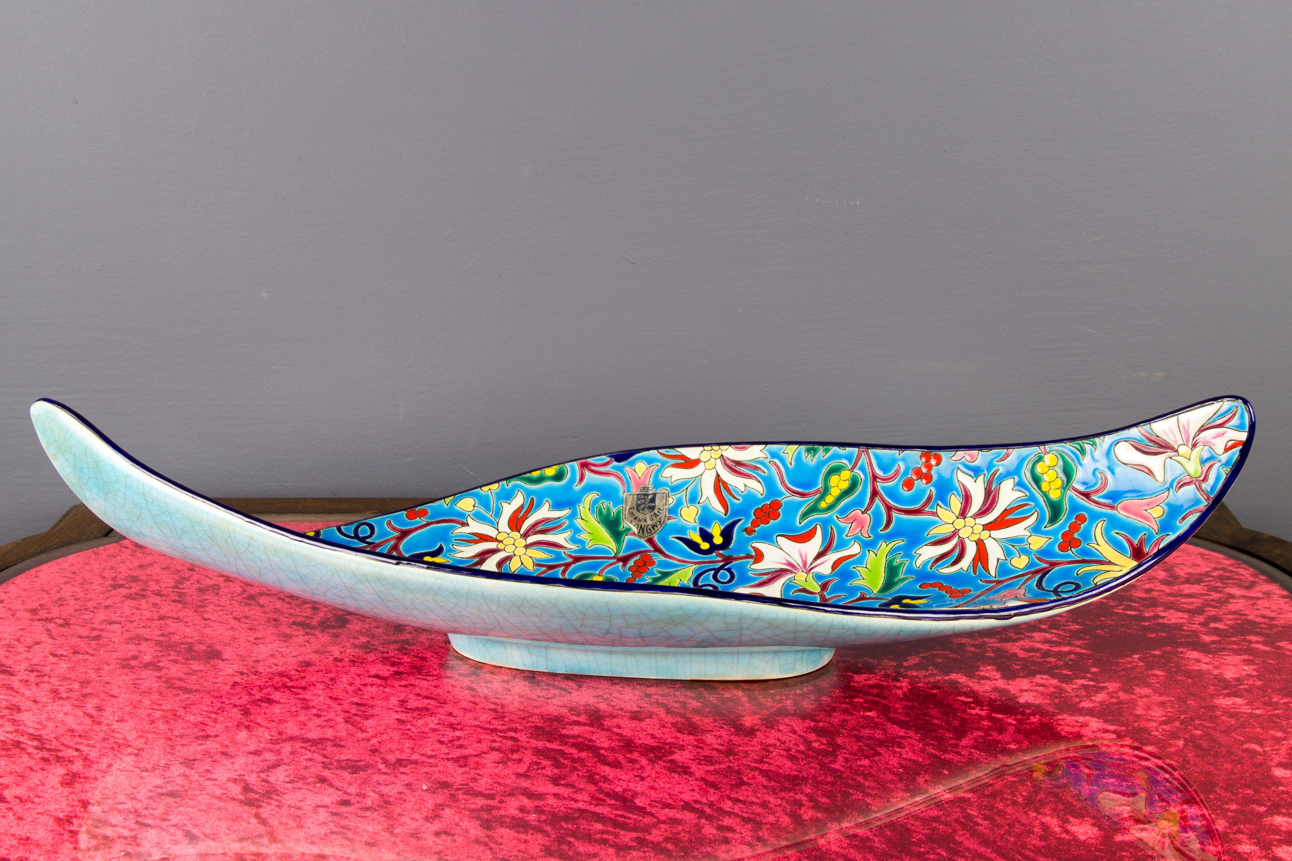 Beautiful French Art Deco style long and oval-shaped earthenware fruit platter by Emaux de Longwy, hand painted and enameled with polychrome floral decoration in white, pink, green, red, blue, and yellow color on blue background. Turquoise ground