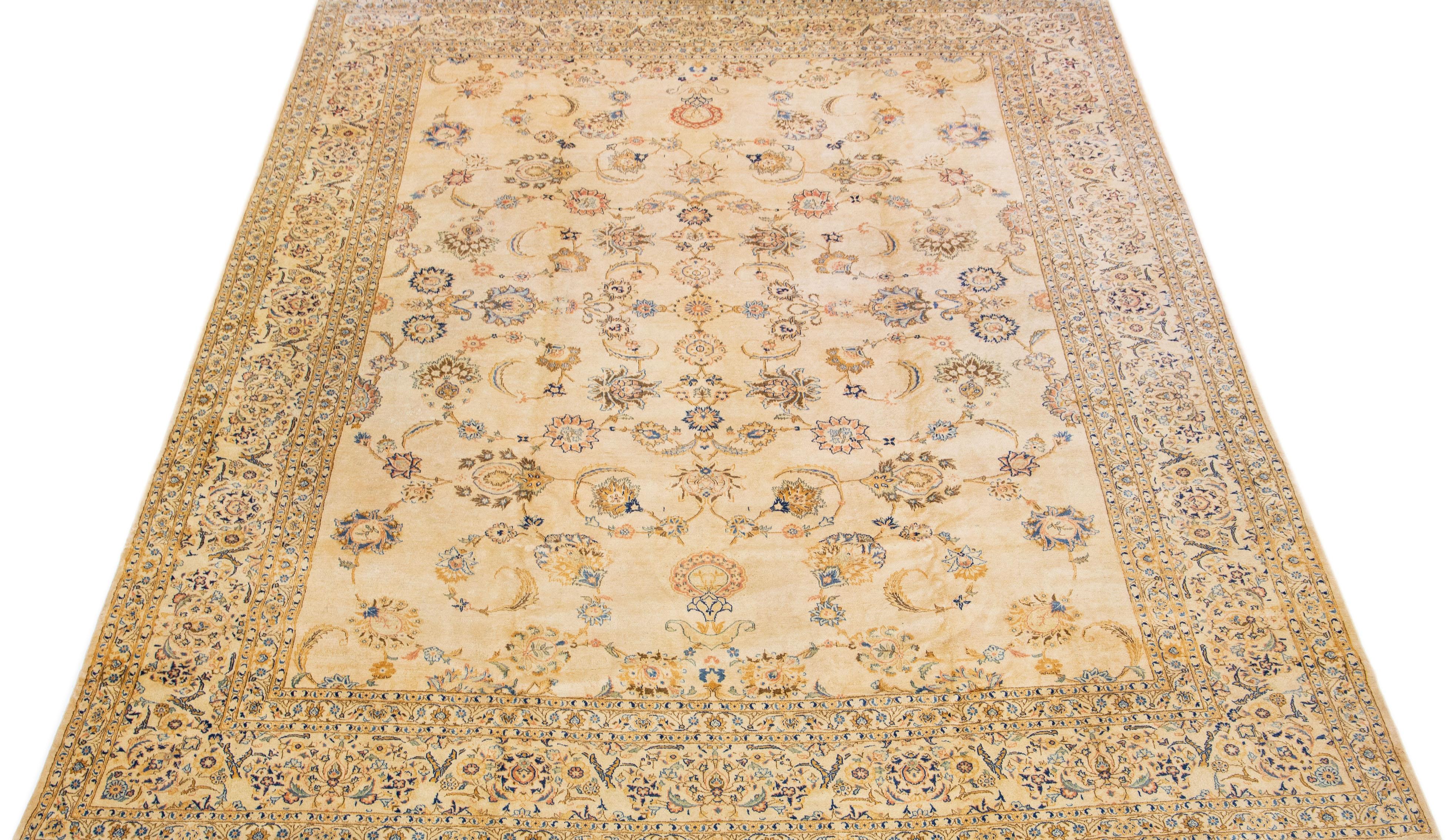 Beautiful Antique Kashan hand-knotted wool rug with a beige color field. This Persian rug has blue, golden, and brown accents in a gorgeous classic floral design. 

This rug measures 10'6