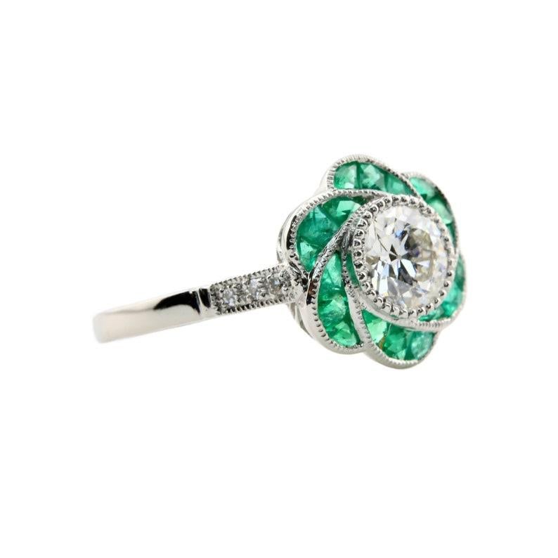 Aston Estate Jewelry Presents:

An Art Deco style flower form diamond, and emerald engagement ring in platinum.

Centered by a 0.85 carat old European cut diamond of H color and VS2 clarity set in a beaded bezel.

Framed by six petals set with