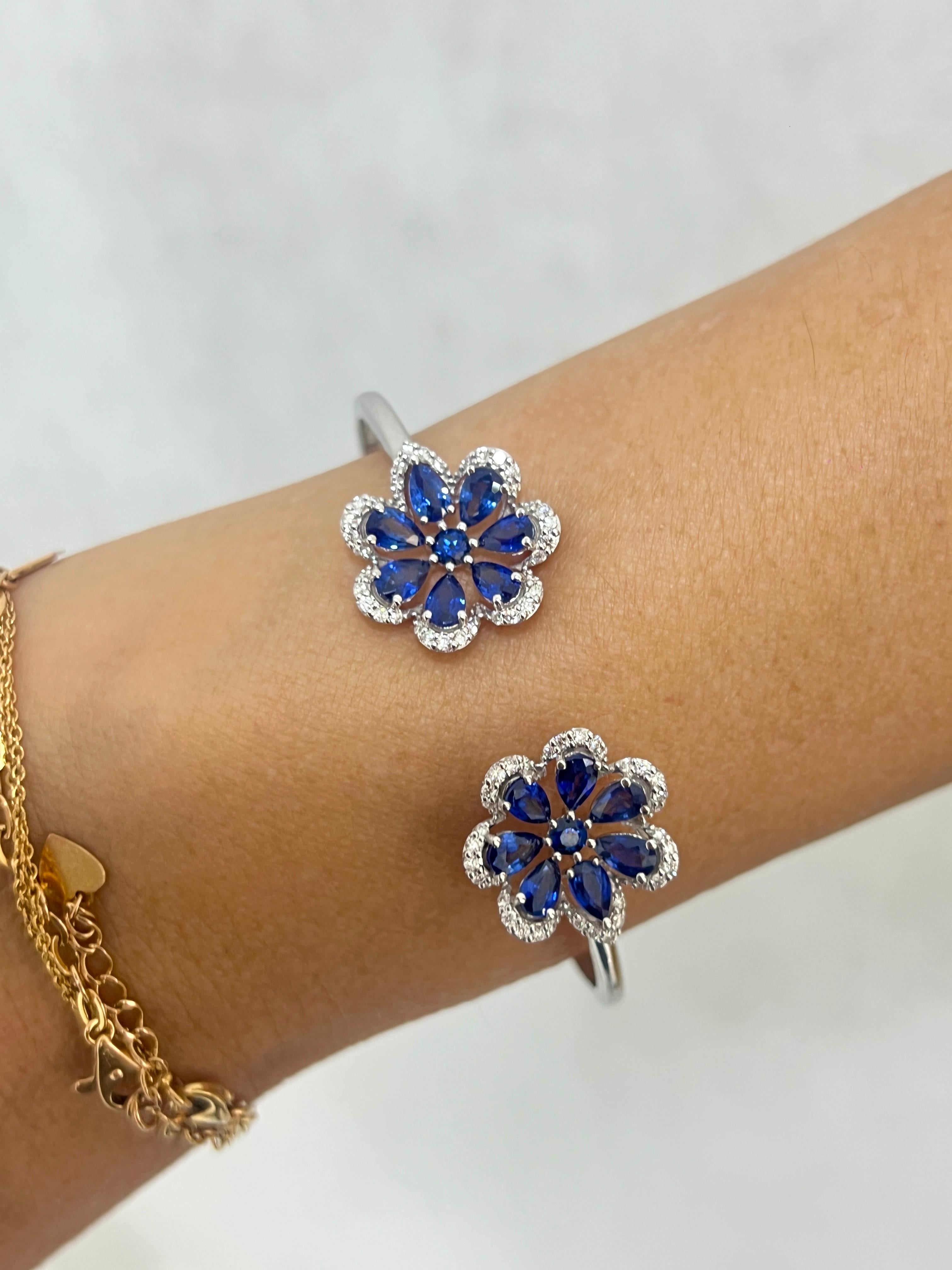 Ce bracelet floral en or 14 carats présente deux motifs floraux exquis sertis de saphirs bleus en forme de poire et rehaussés d'un halo de diamants. Conçu dans un style manchette ouverte, le bracelet met en valeur la beauté naturelle des saphirs