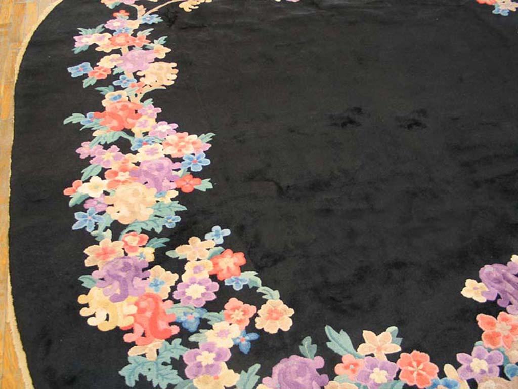 A colourful floral wreath stands out in this borderless black ground Chinese Art Deco carpet, circa 1930 from Peking (Beijing).The seasonal flowers are detailedv in bluers, oranges, yellows and ivory. Thin stems support the blossoms. The effect is