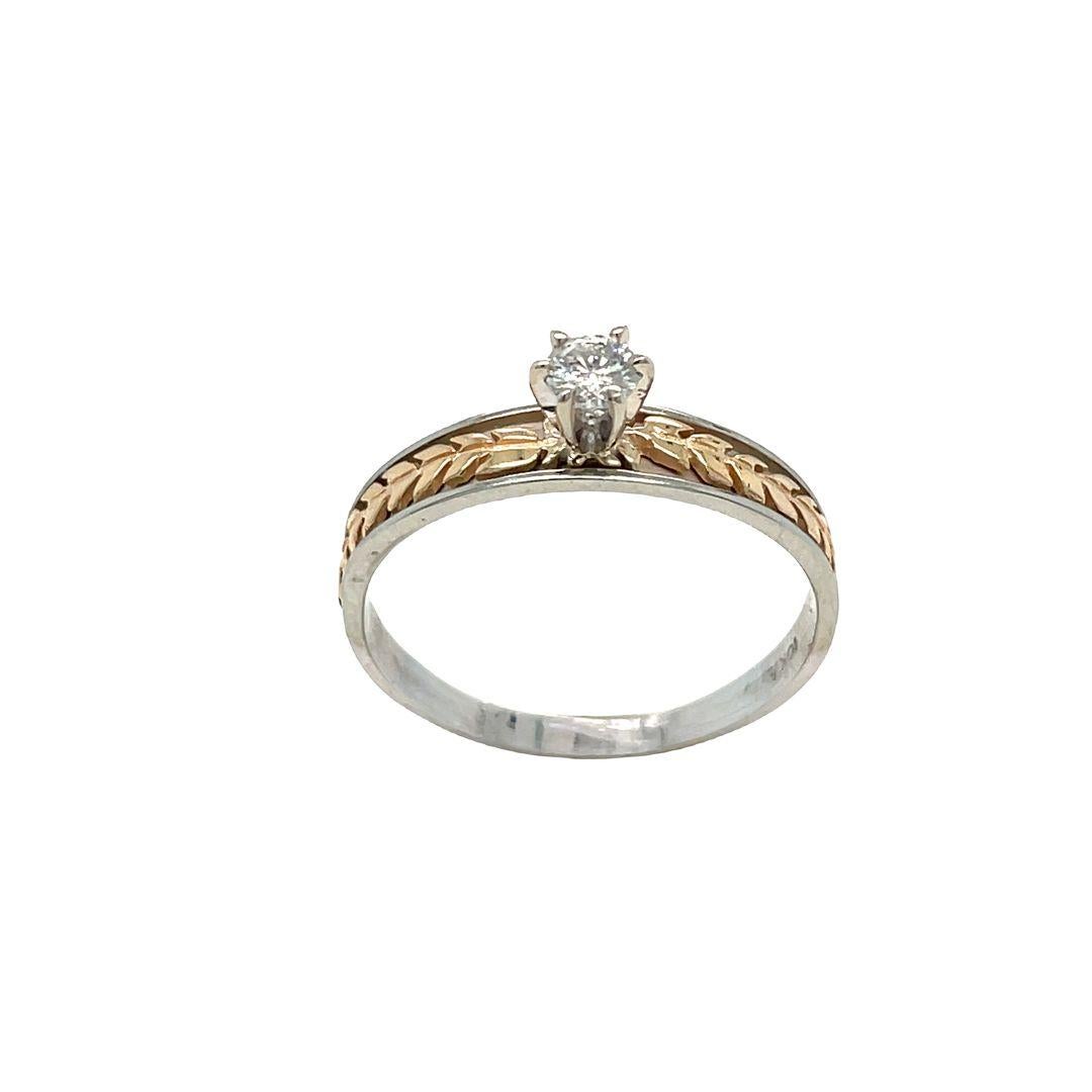This antique diamond engagement ring features a 6-prong set round one round brilliant cut diamond  and two tone leaf floral motif design along the shank. Diamond is weighing 0.15 carat with a clarity of SI2 and a color grade of I. 
This lovely