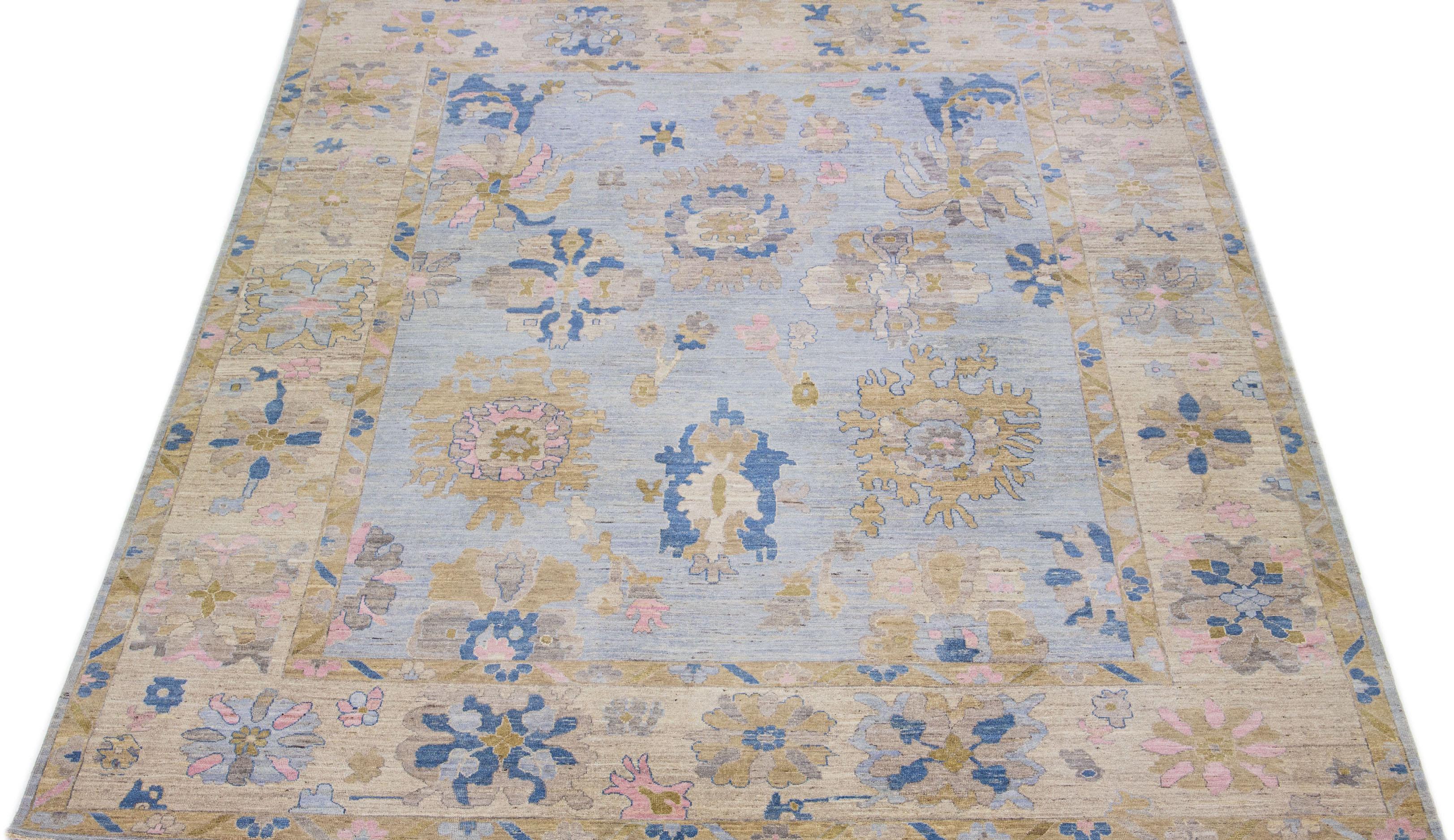This contemporary Oversize Oushak Style rug boasts a hand-knotted wool construction, complemented by a charming light blue color. Its tastefully crafted frame showcases lovely floral motifs in a fascinating blend of brown, pink, and blue