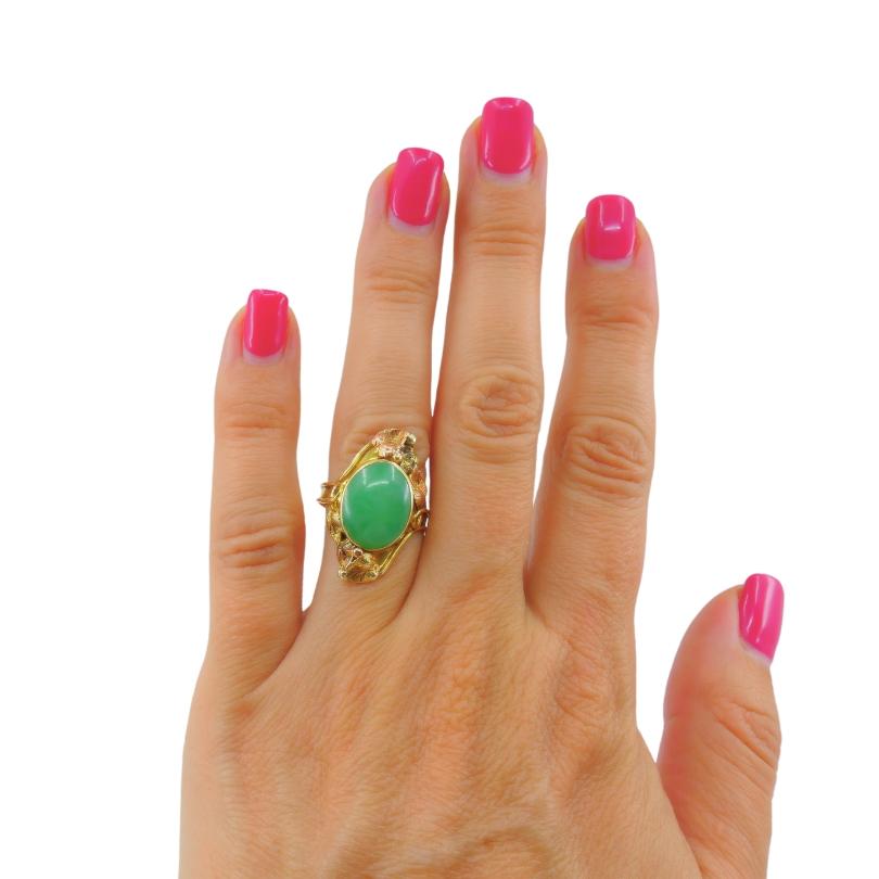 A floral design jade ring, crafted in two-tone 14k gold. This antique jade ring beautifully showcases the organic design elements of the Art Nouveau period. An oval jade stone is bezel set in 14k gold, with the delicate and detailed surrounding