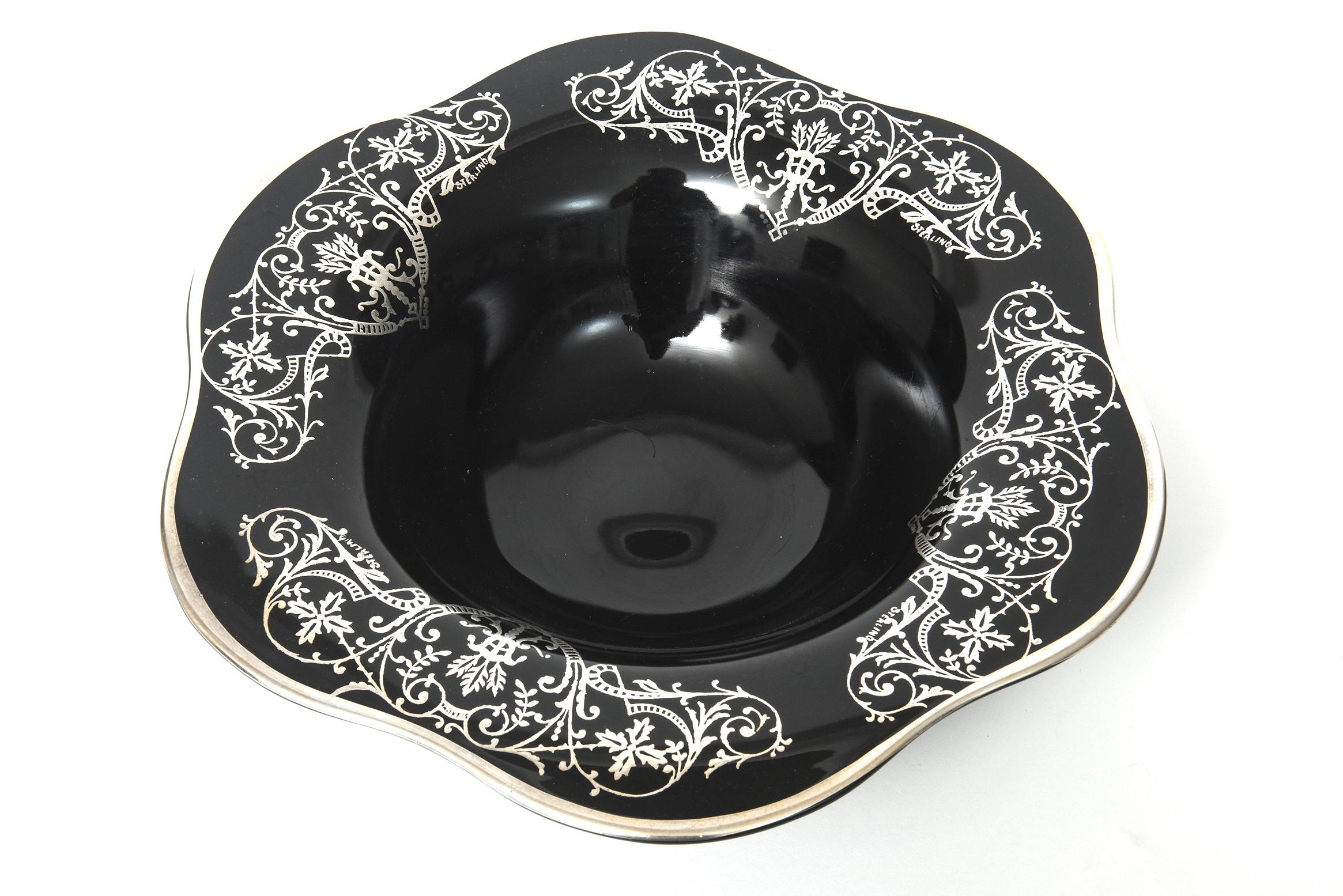 Dramatic early 20th century sterling silver overlay three footed bowl featuring a foliate cartouche leaf, flower and scroll design on a rare flower shaped shiny ebony black glass bowl.  The bowl sits on three legs that end in rounded feet.  Each of