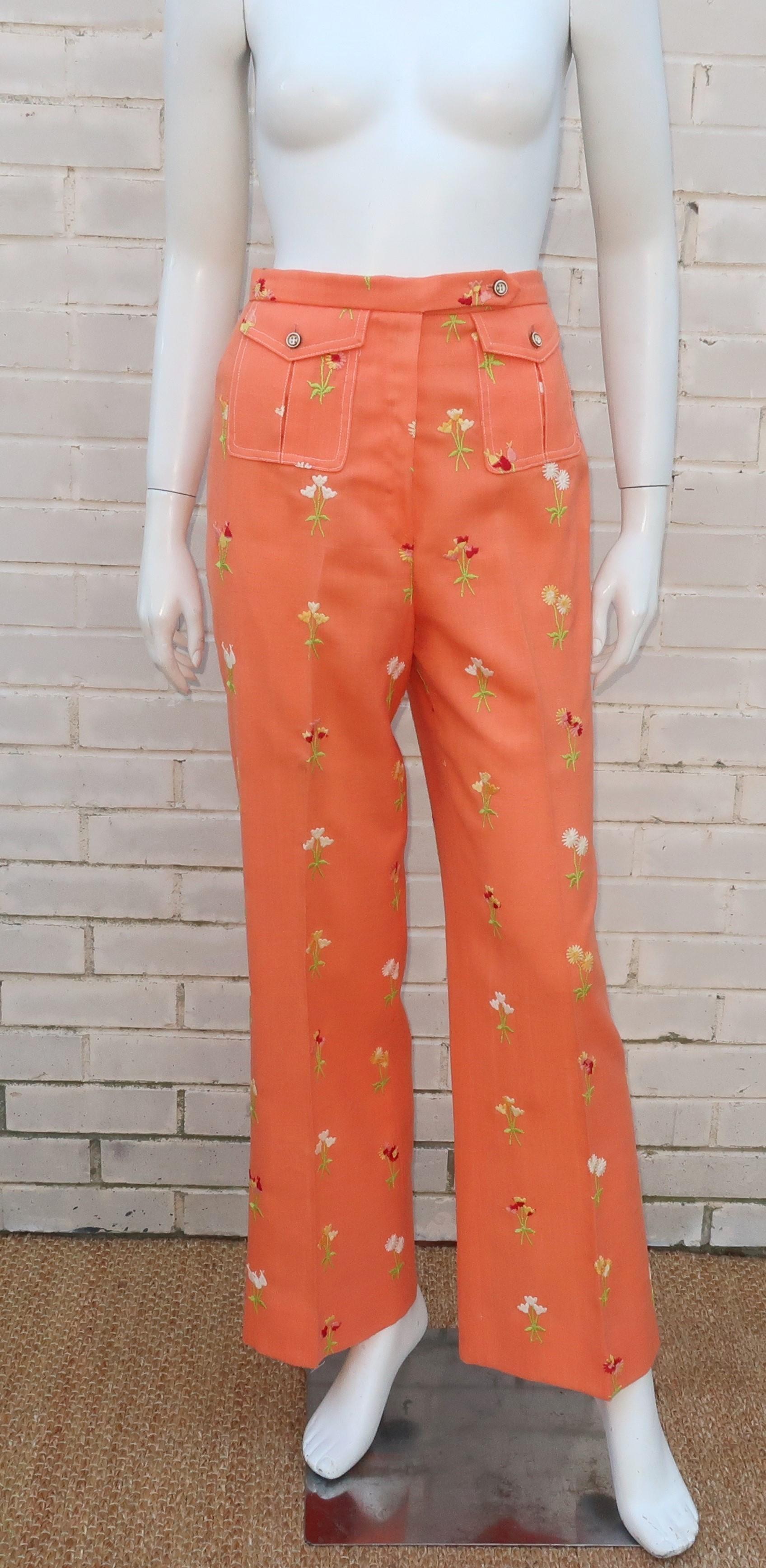 1970's peachy orange nubby linen pants with embroidery depicting wildflowers in shades of red, white, yellow, peach and green.  The high waist silhouette zips and buttons with tab waistband and has full legs with a slight flare at the hem.  The flap