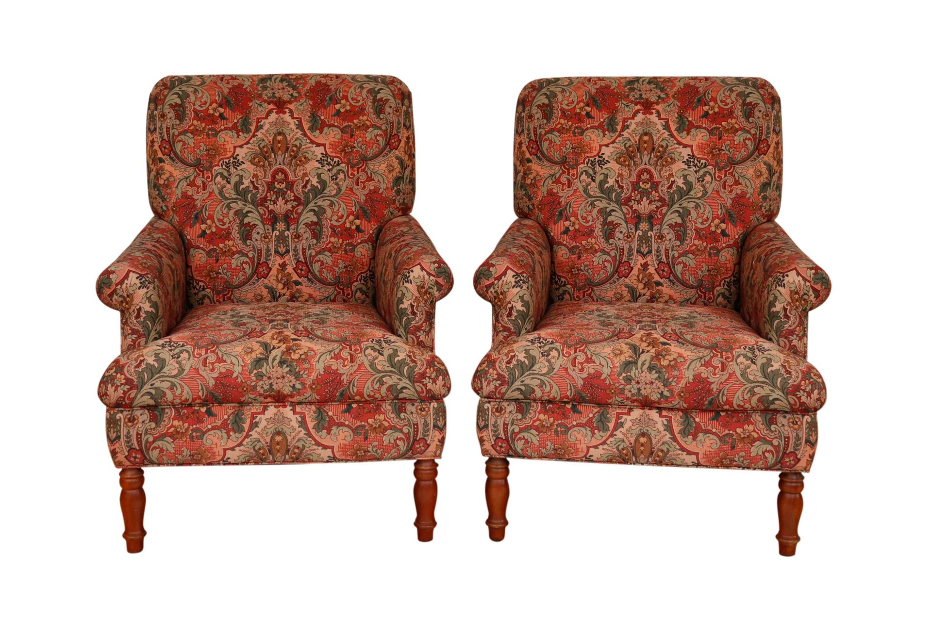 A pair of English style lounge chairs. Upholstered in a rich Ishana style floral printed cotton with bunches of acanthus foliage repeated in red, sage, mocha and olive on a blush ground. The seat back reclines with a flat crest rail and pleated arms