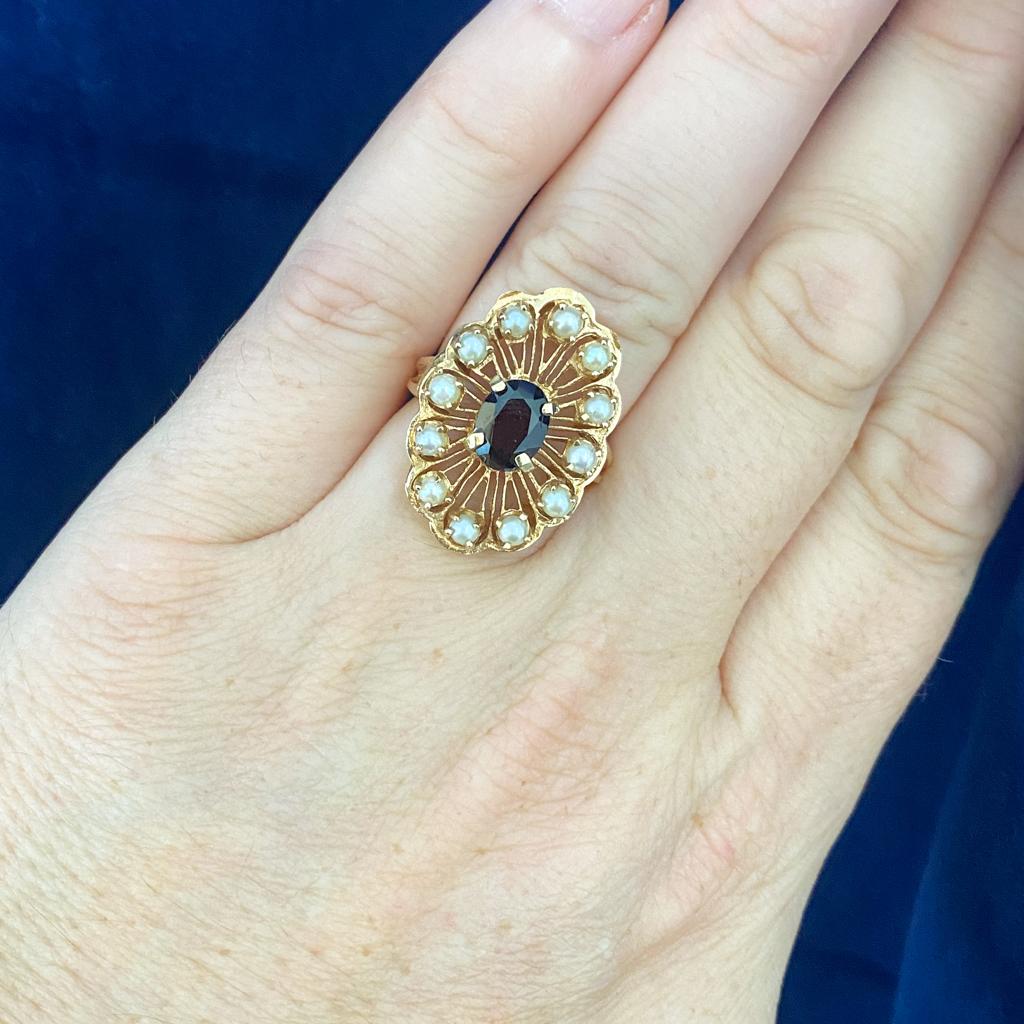 A lovely oval garnet sits proudly at the center of this beautiful wirework ring top with floral crescent edges, each scallop set with a beautiful cultured pearl. The matched cultured pearls add a beautiful shimmer to the floral outline of the ring